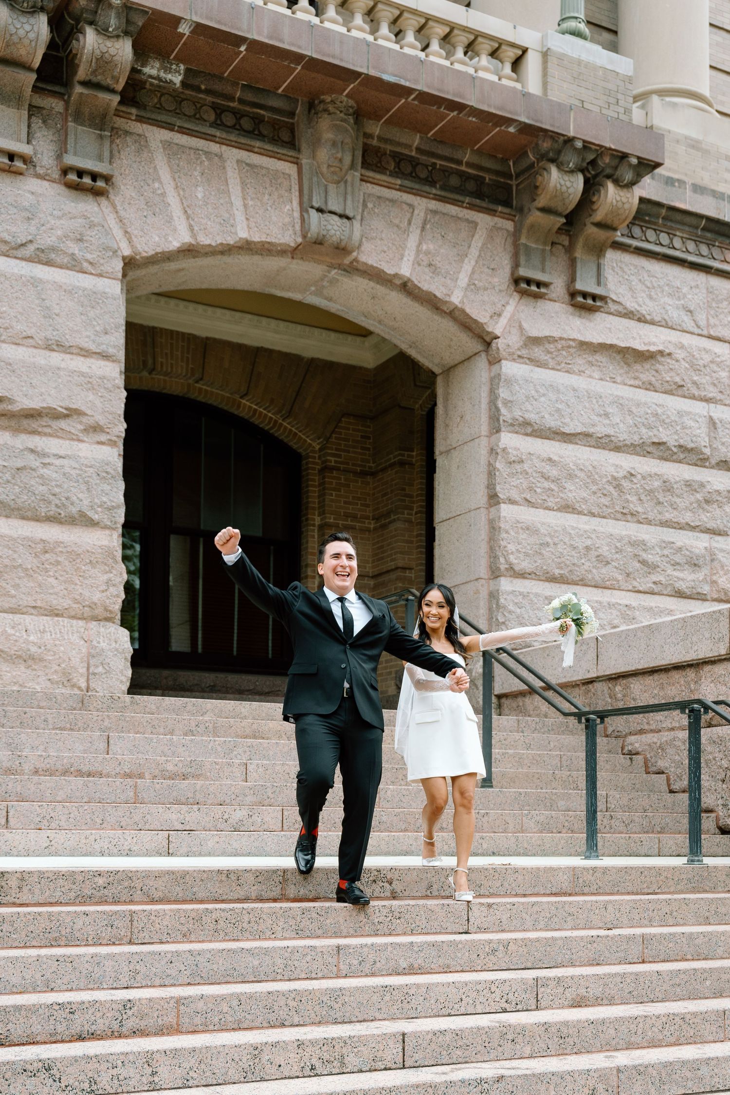 Wedding couple celebrating on grand stone steps of historic building.