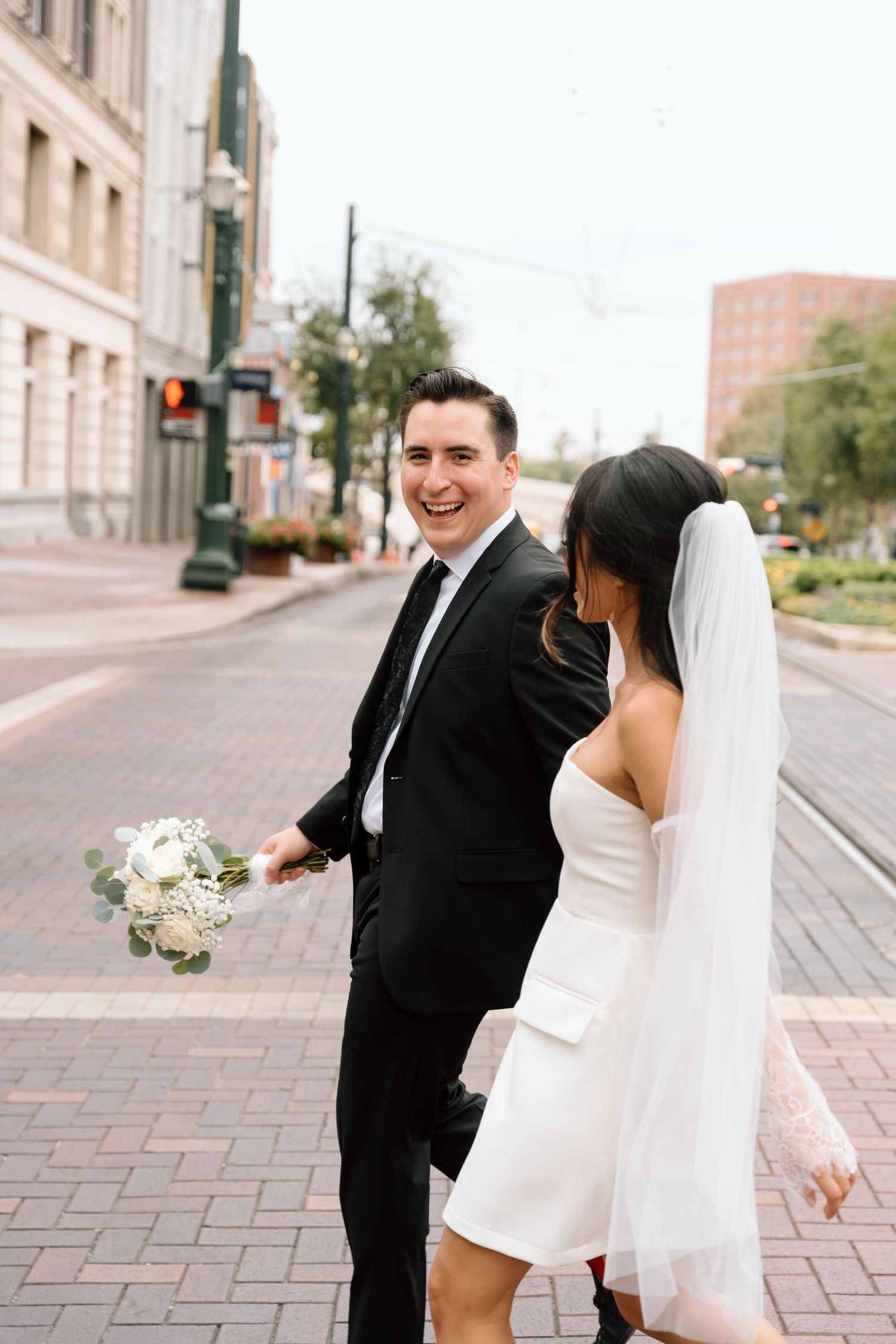 Newlyweds dancing and laughing together on brick paved street.