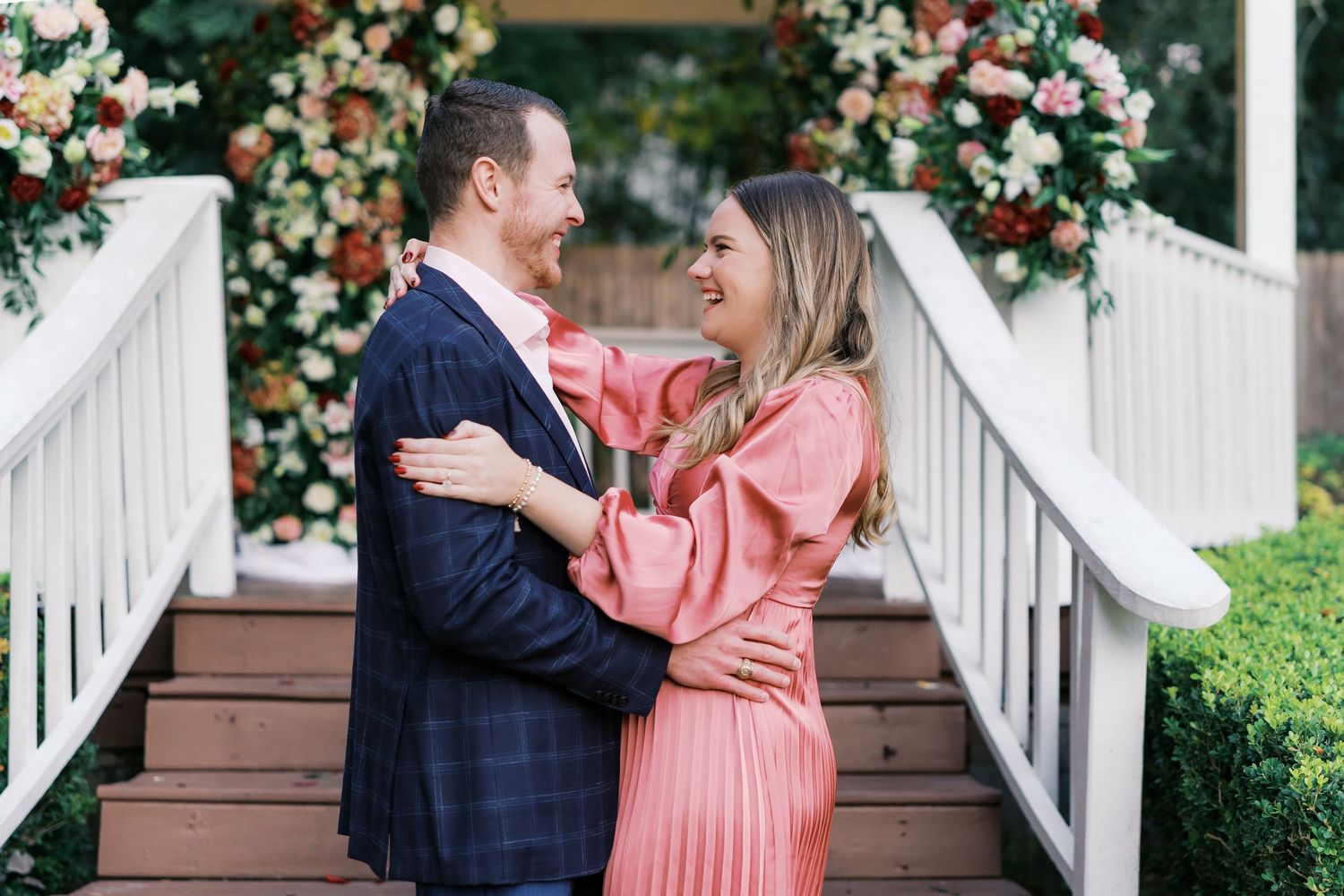 A couple laughs together on a gazebo porch surrounded by floral arrangements.