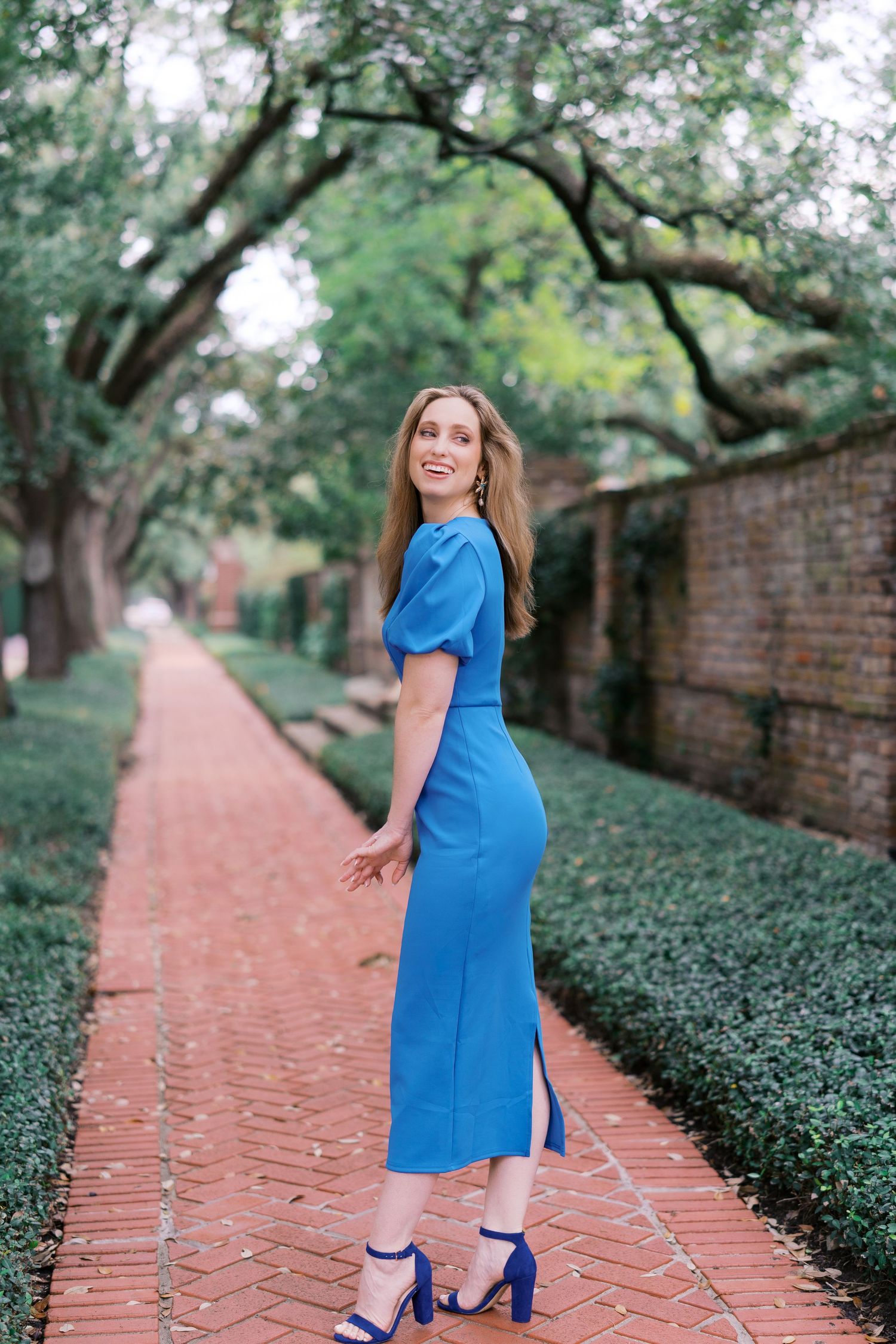 Elegant maternity photos taken on a brick pathway surrounded by lush greenery.