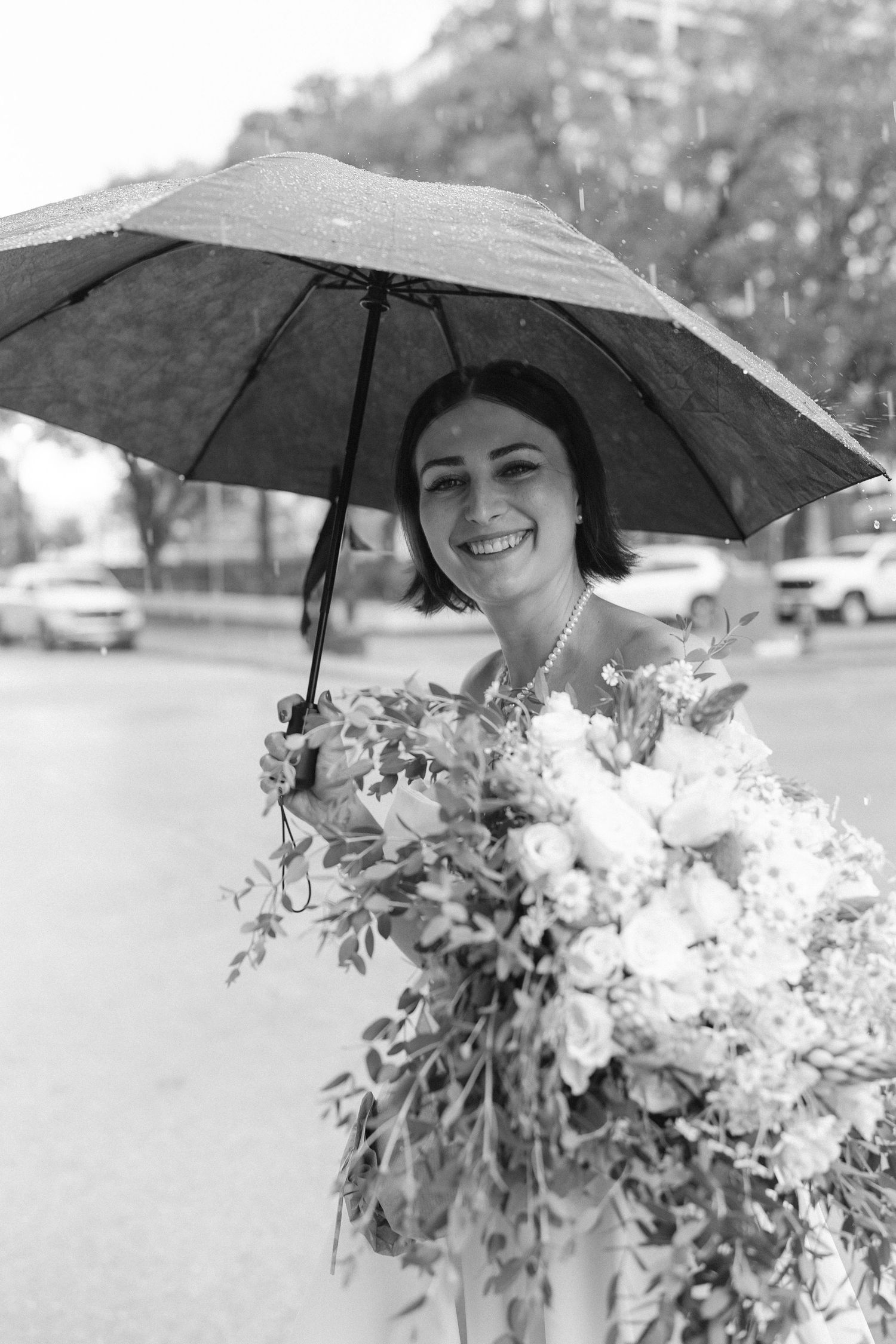 Black and white photo of wedding party with umbrellas and floral bouquets.