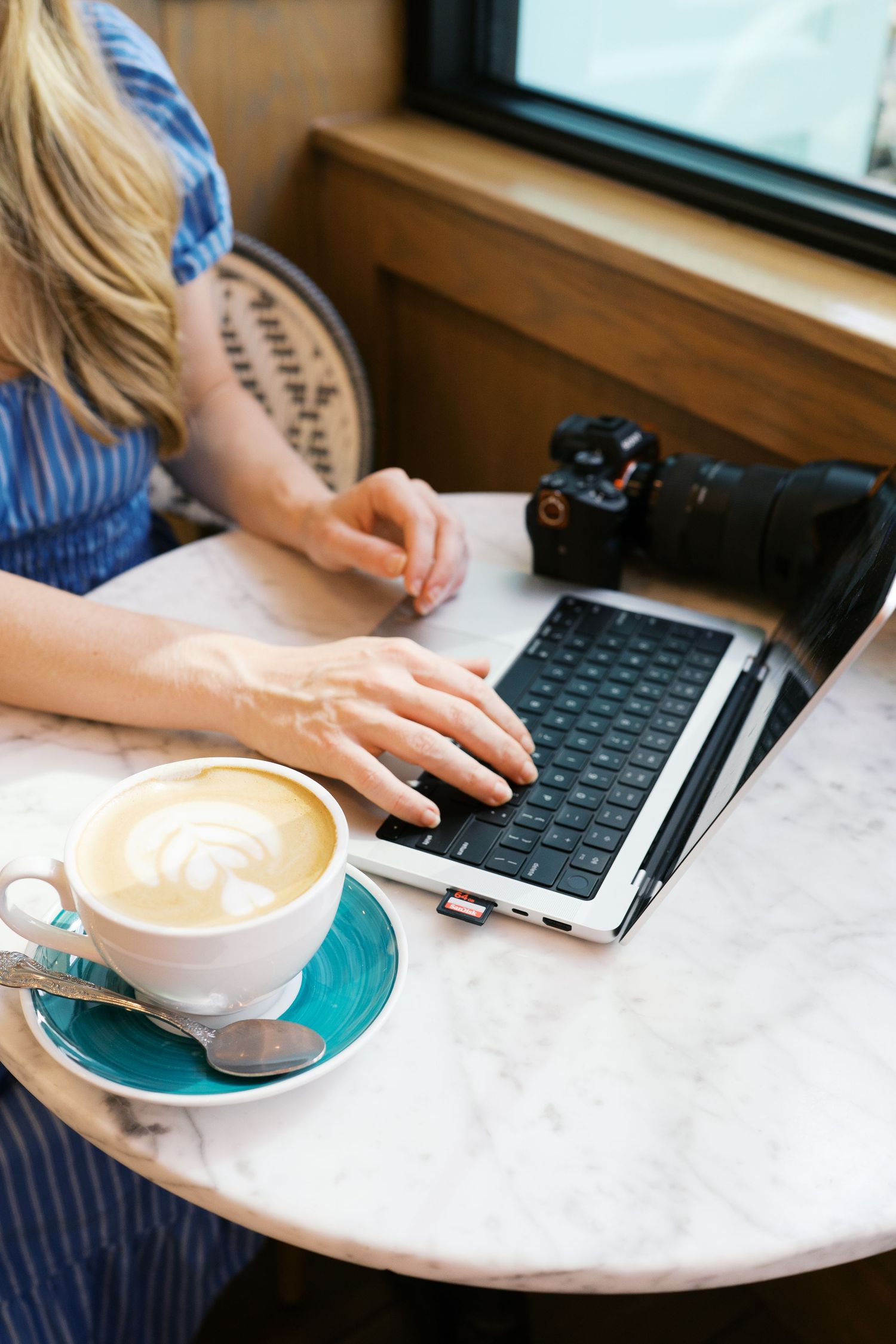 Person working on laptop with coffee at marble table in cafe setting.