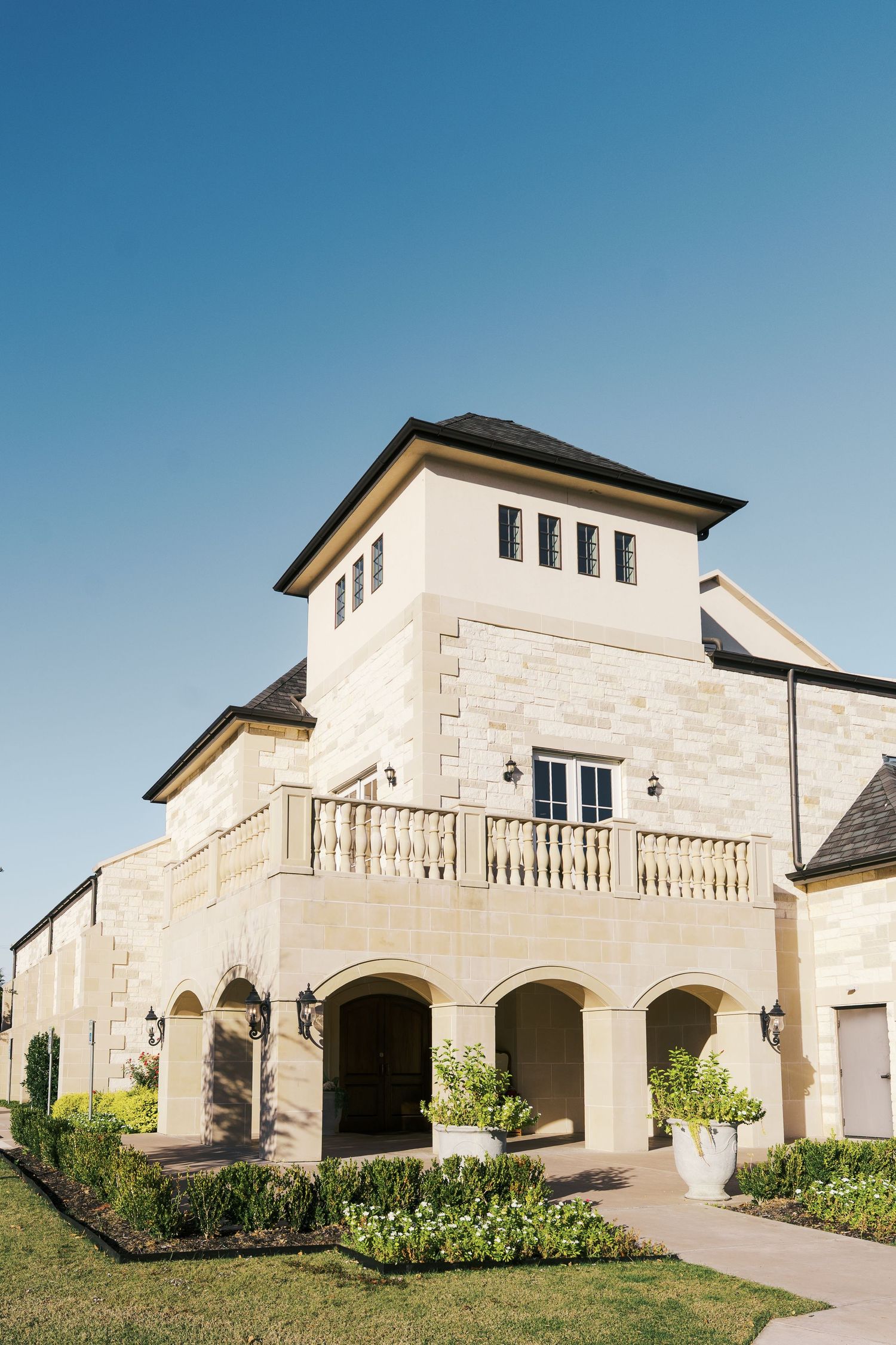 Modern white stone wedding venue exterior with arched entryways under bright blue sky.