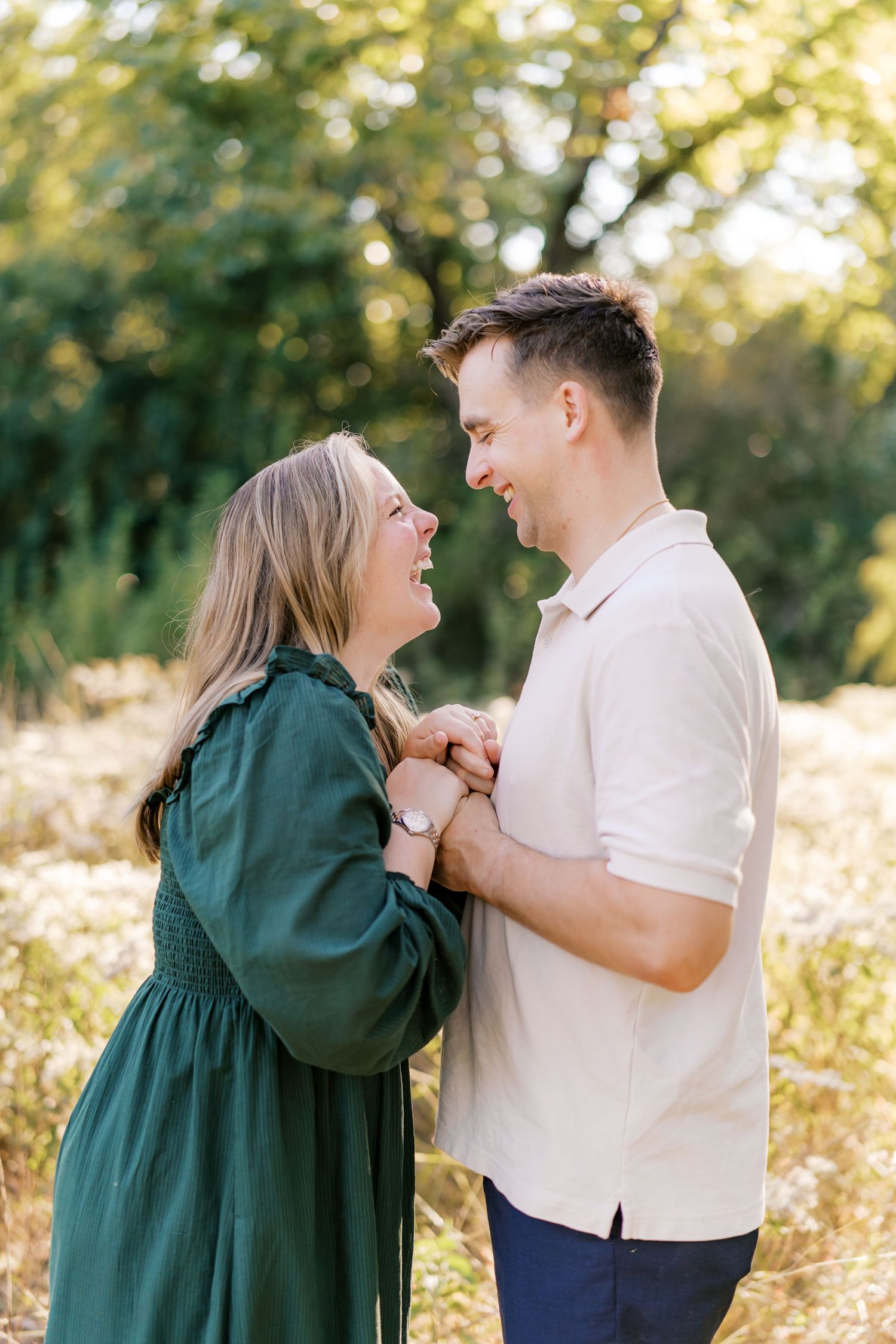 A couple shares a joyful moment together in a sunlit field wearing casual attire.