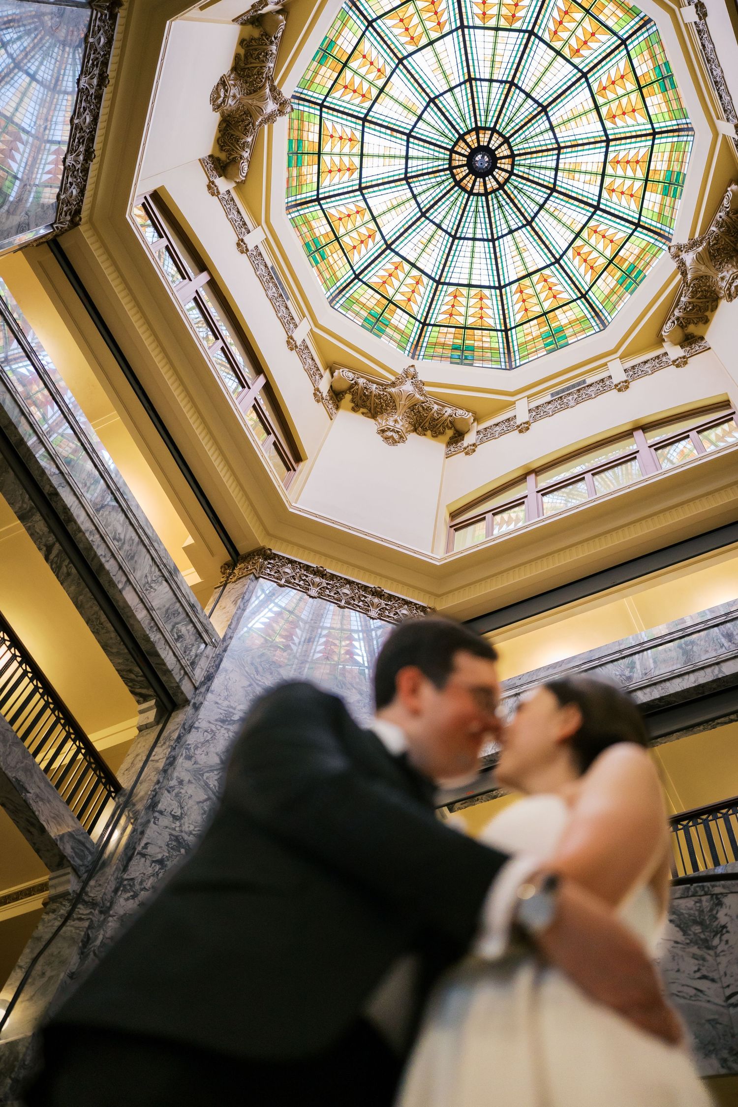 Wedding photos under an ornate stained glass dome ceiling in historic building.