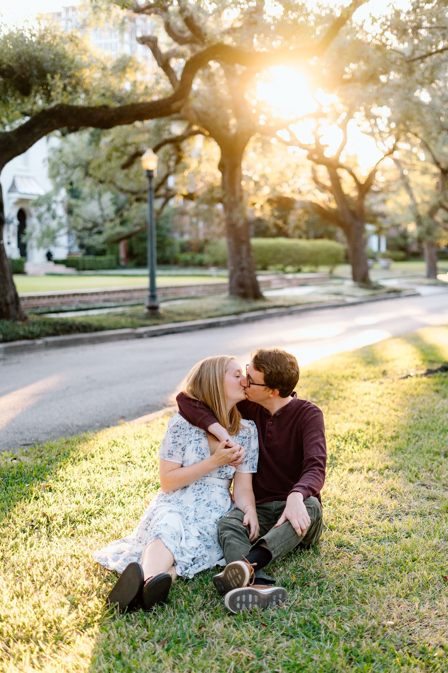 A couple relaxes on grass under oak trees during golden hour.