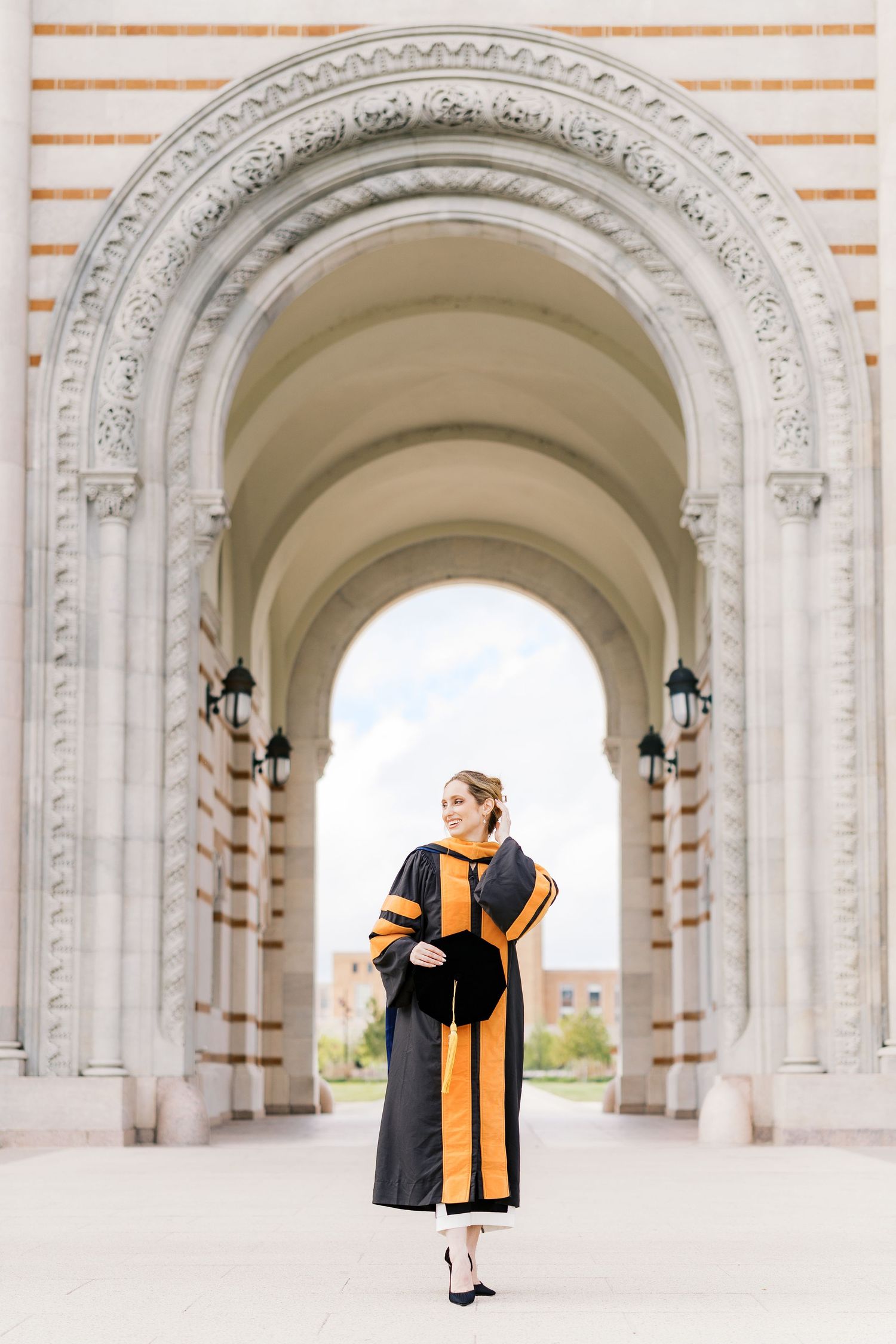 Graduate in academic regalia stands centered in ornate white stone archway.
