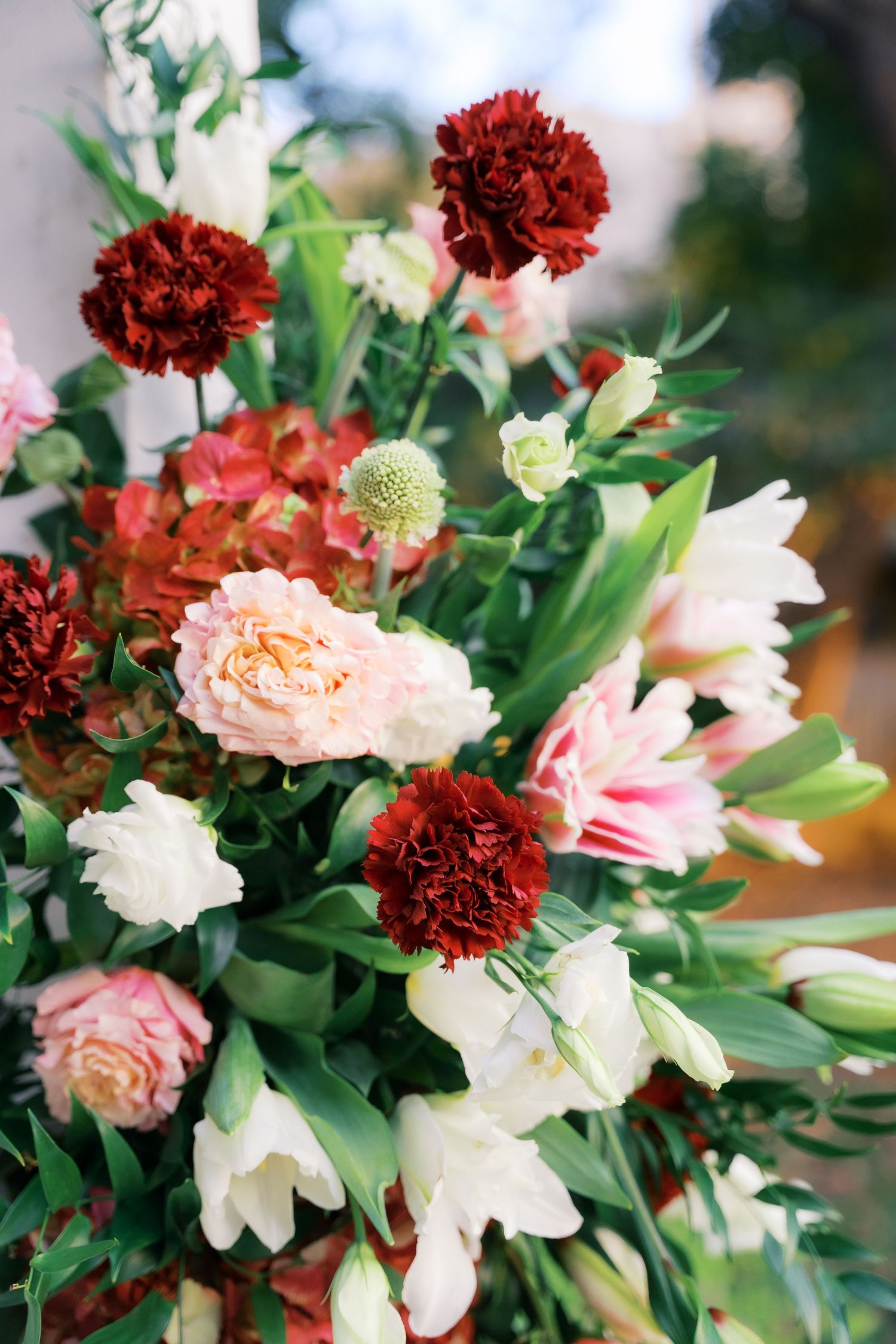 Close-up of romantic floral arrangement with white lilies, burgundy carnations, and pink roses.