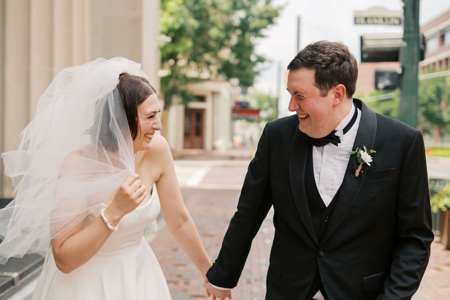 Couple shares candid moments during their wedding photoshoot along a brick pathway.
