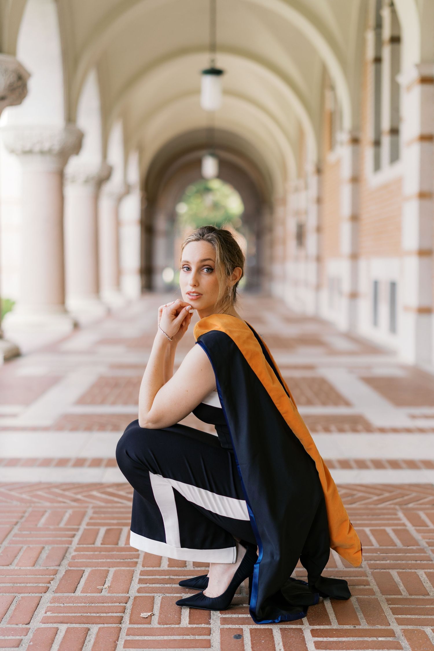 Professional photoshoot in an ornate colonnade featuring black attire and orange accents.