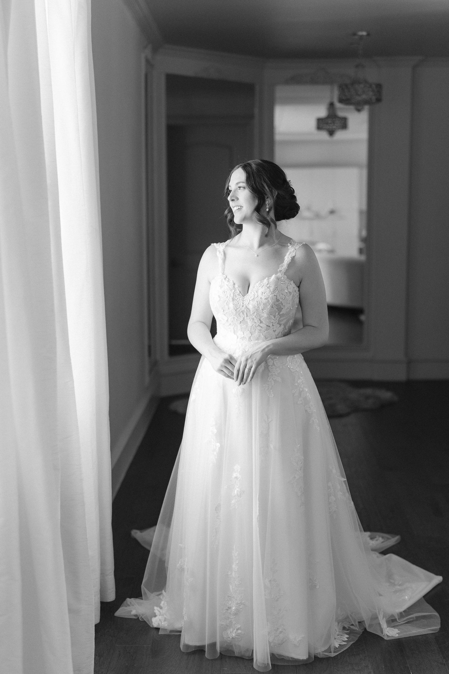 A bride in an elegant white wedding gown stands in a softly lit room.