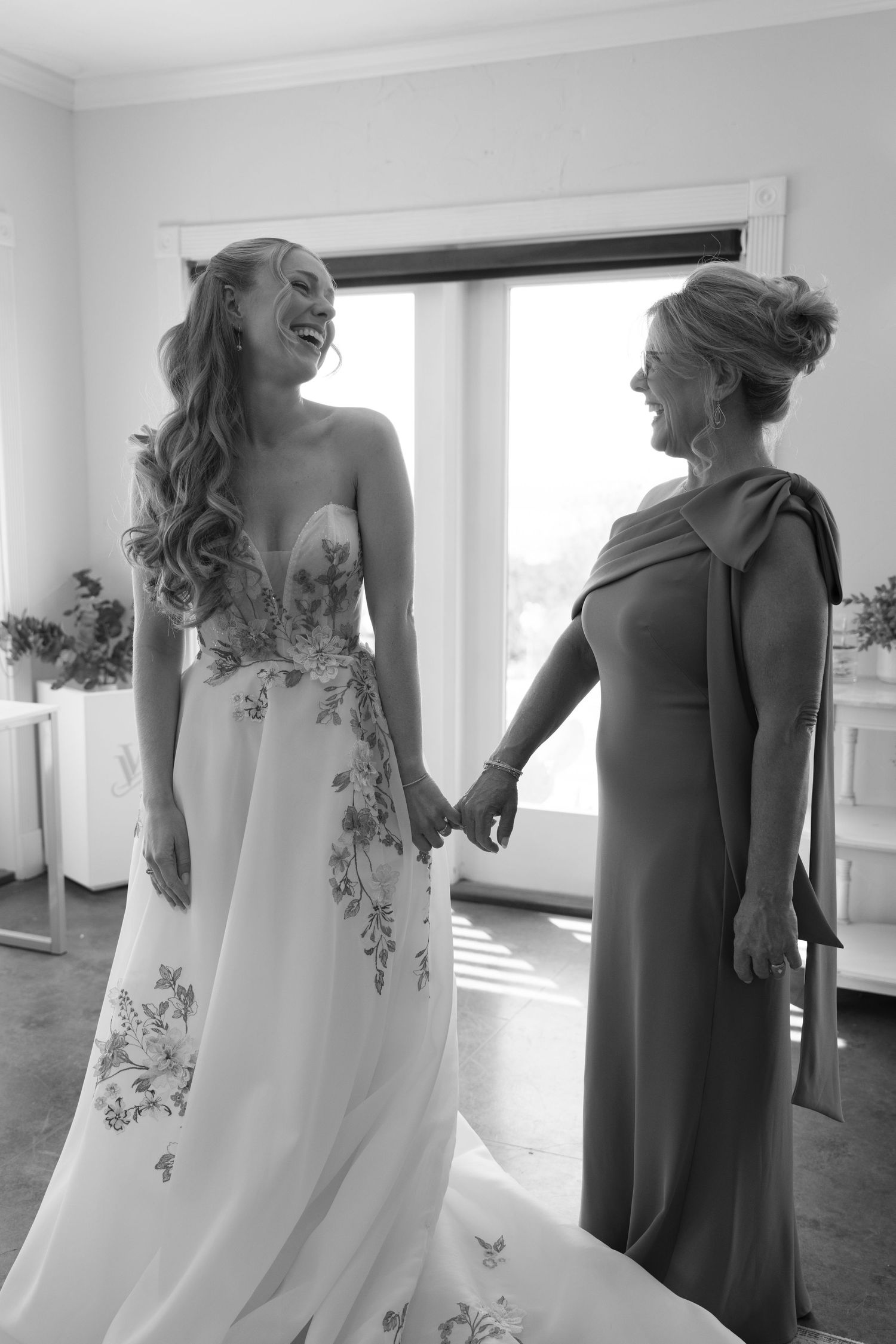 Row of bridesmaids in elegant white and gray dresses standing in a bright room.