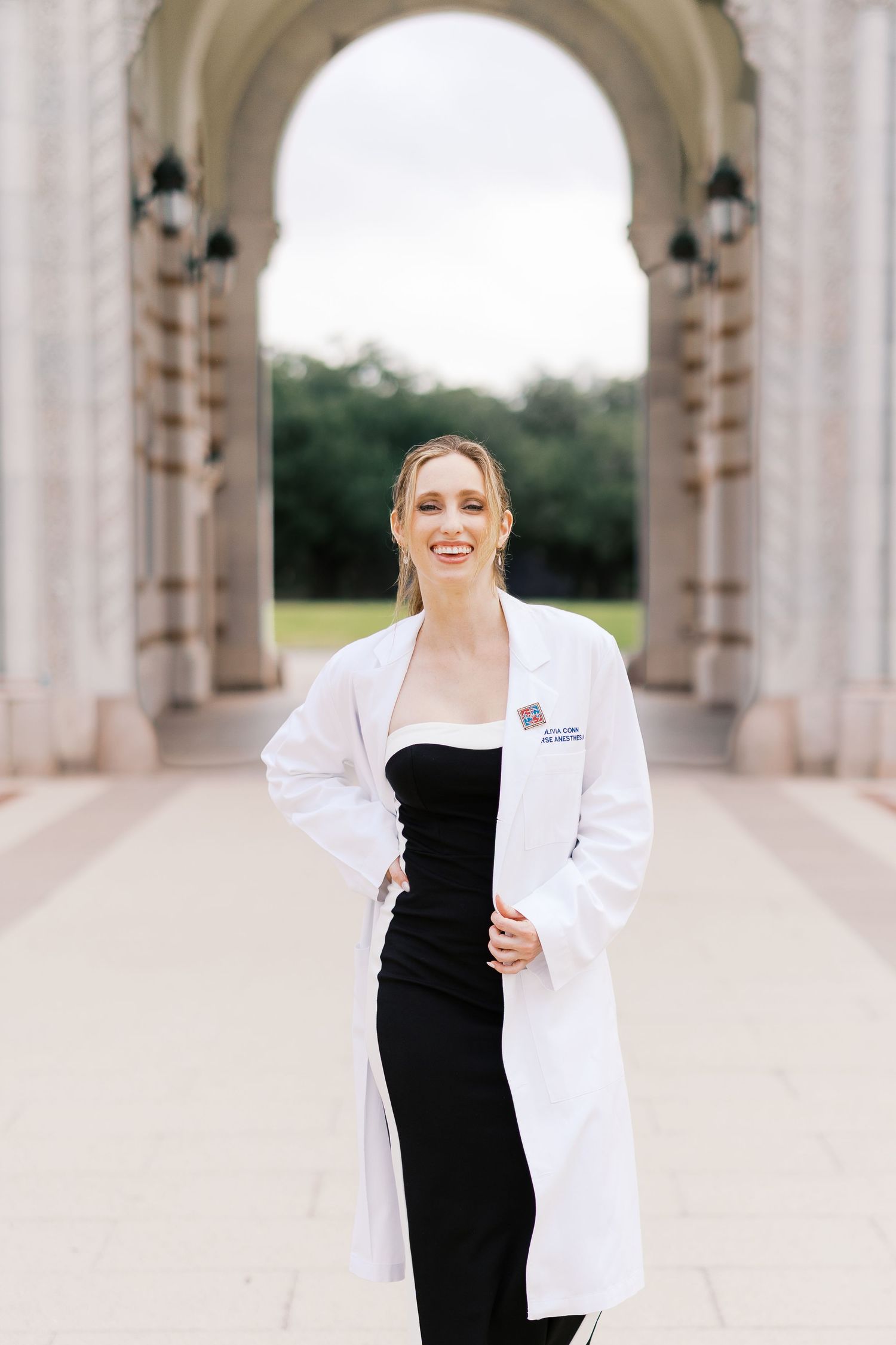 Professional in white coat and black dress poses in ornate archway.