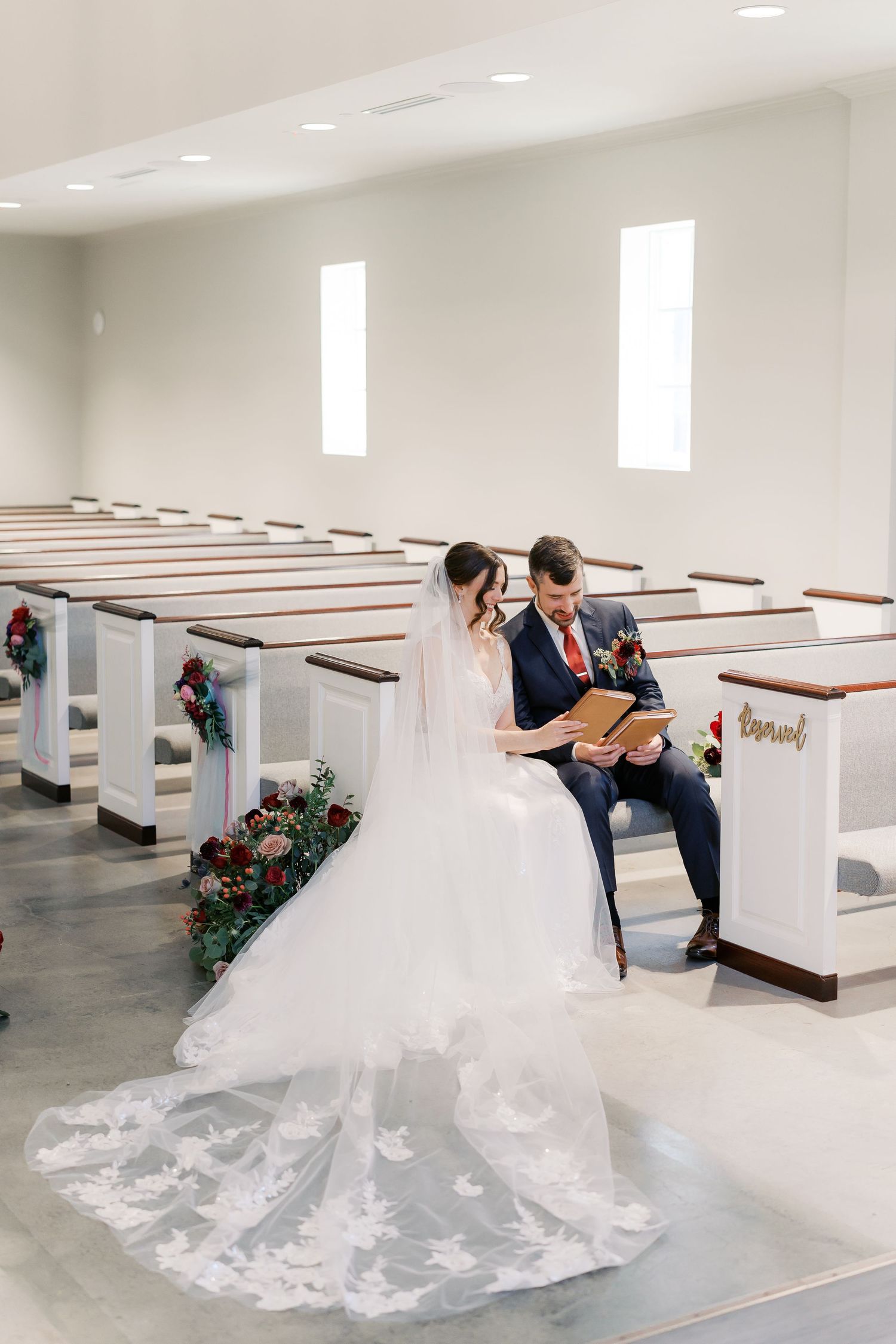 A wedding couple embraces in a church sanctuary with wooden pews and floral arrangements.