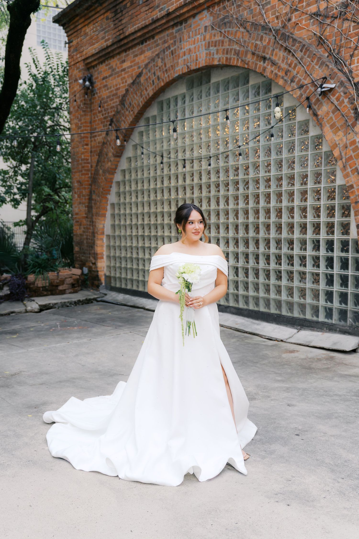 Bridal portrait series under brick archways featuring an elegant off-shoulder white wedding gown.