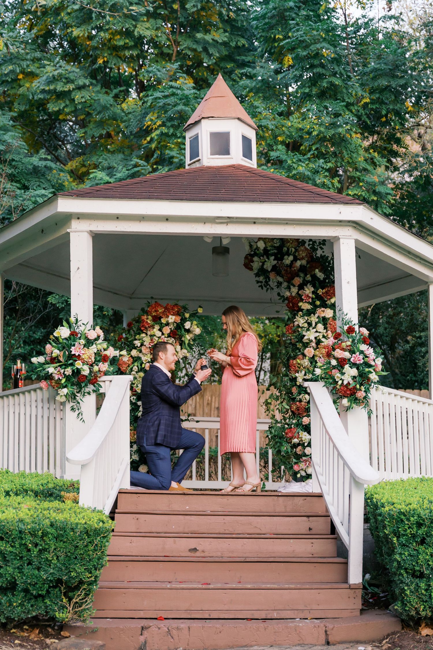 A couple shares an intimate moment on a decorated gazebo platform surrounded by summer foliage.