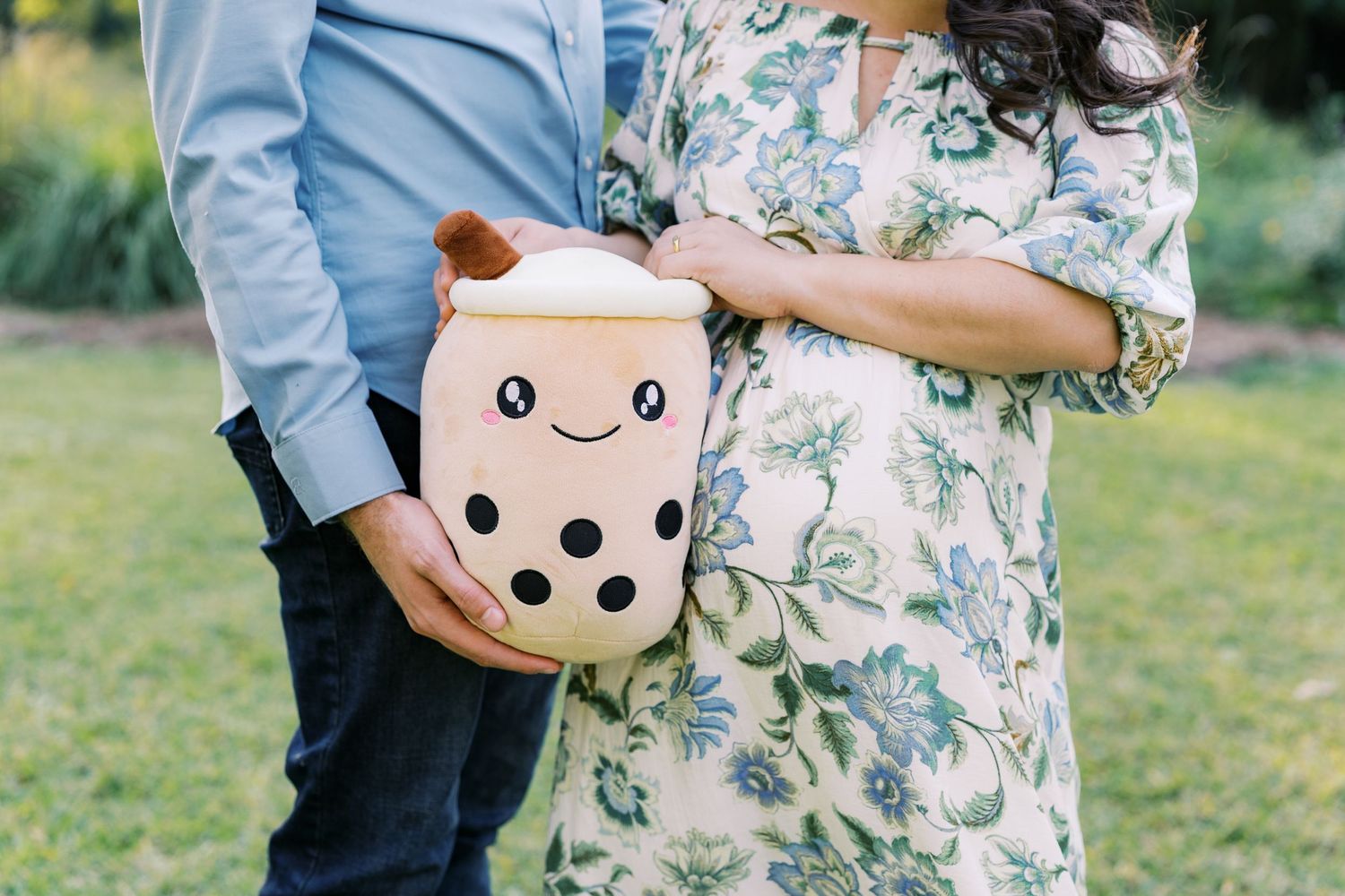 A couple in floral and blue attire stands together in a sunny outdoor setting.