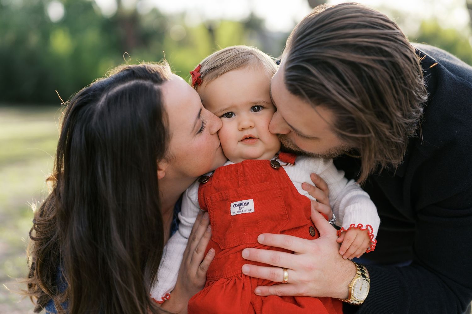 Parents sharing tender moment with baby during outdoor family photoshoot.
