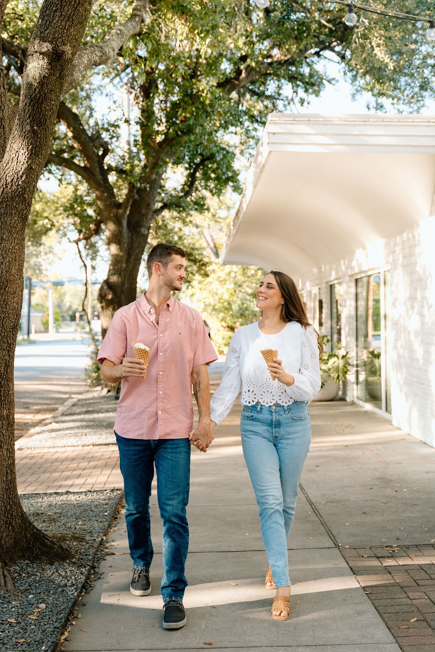 Couple walking together on a tree-lined brick pathway while enjoying ice cream cones.