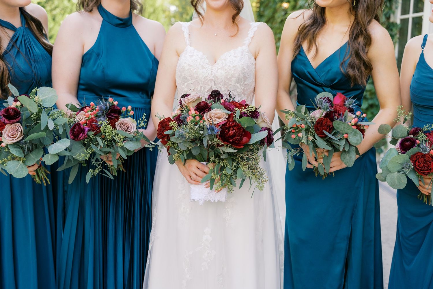 Close-up of bridal party holding burgundy and green bouquets with teal dresses.