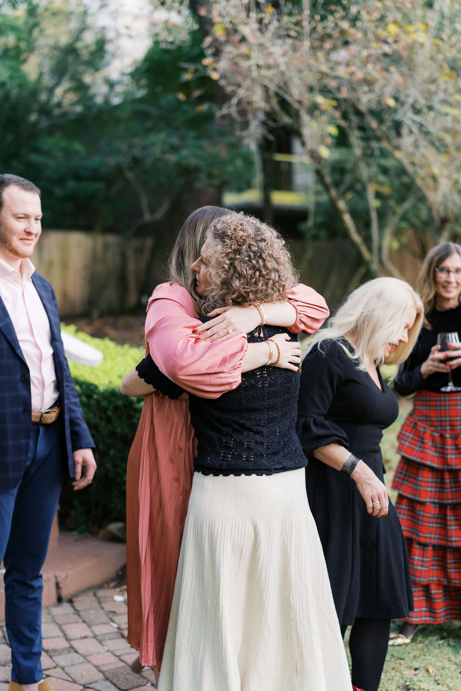 A group embraces during an outdoor gathering near a brick pathway.