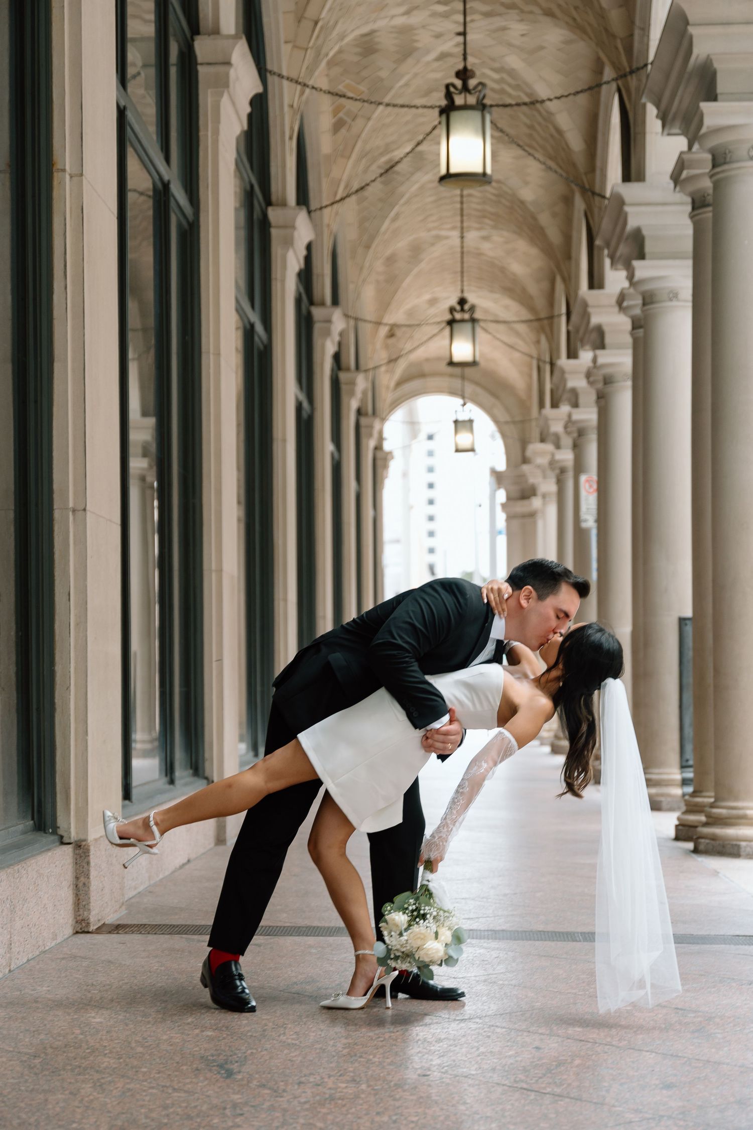 Wedding couple posing playfully in arched colonnade hallway.