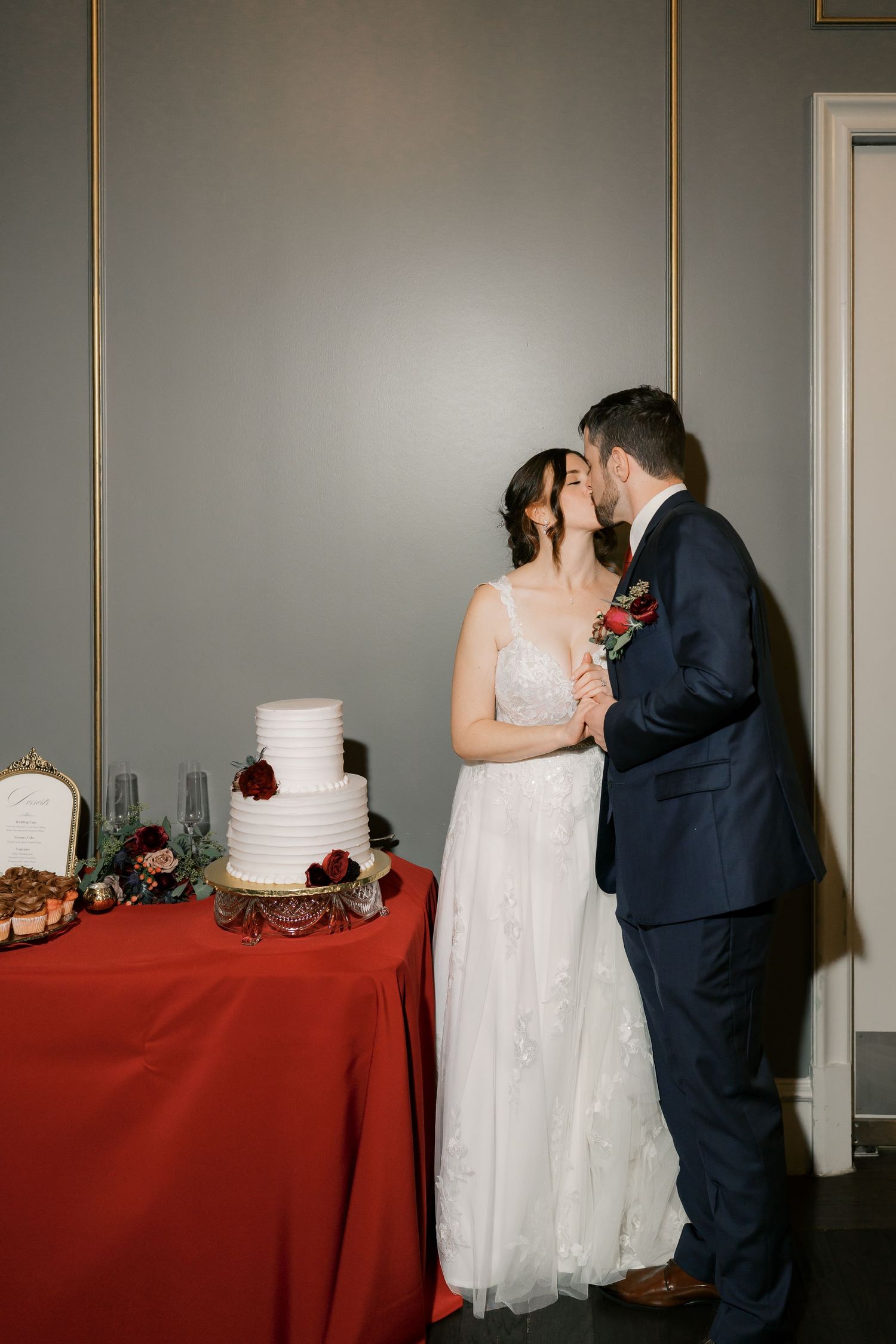 Newlyweds stand beside their wedding cake table during the reception.