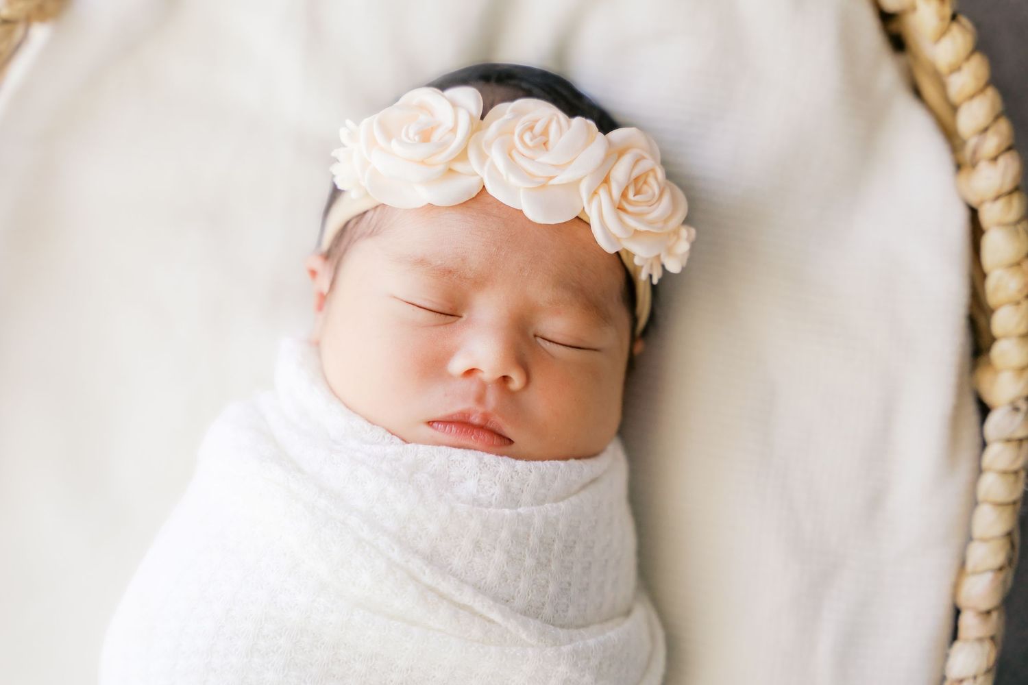 A sleeping newborn wearing a delicate peach rose crown headband.