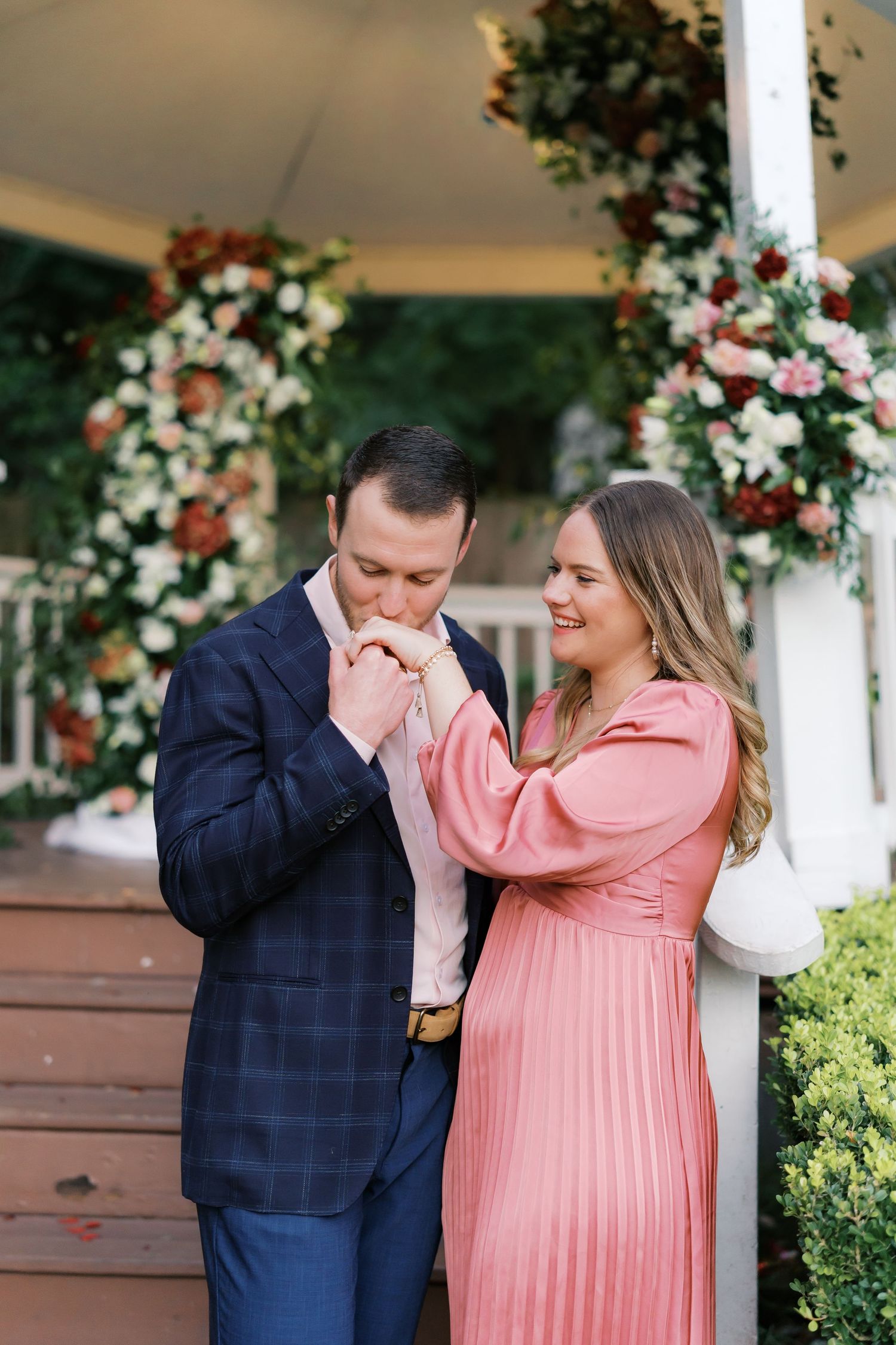 A romantic engagement photo series showing a couple embracing, with the woman wearing a pink pleated dress.