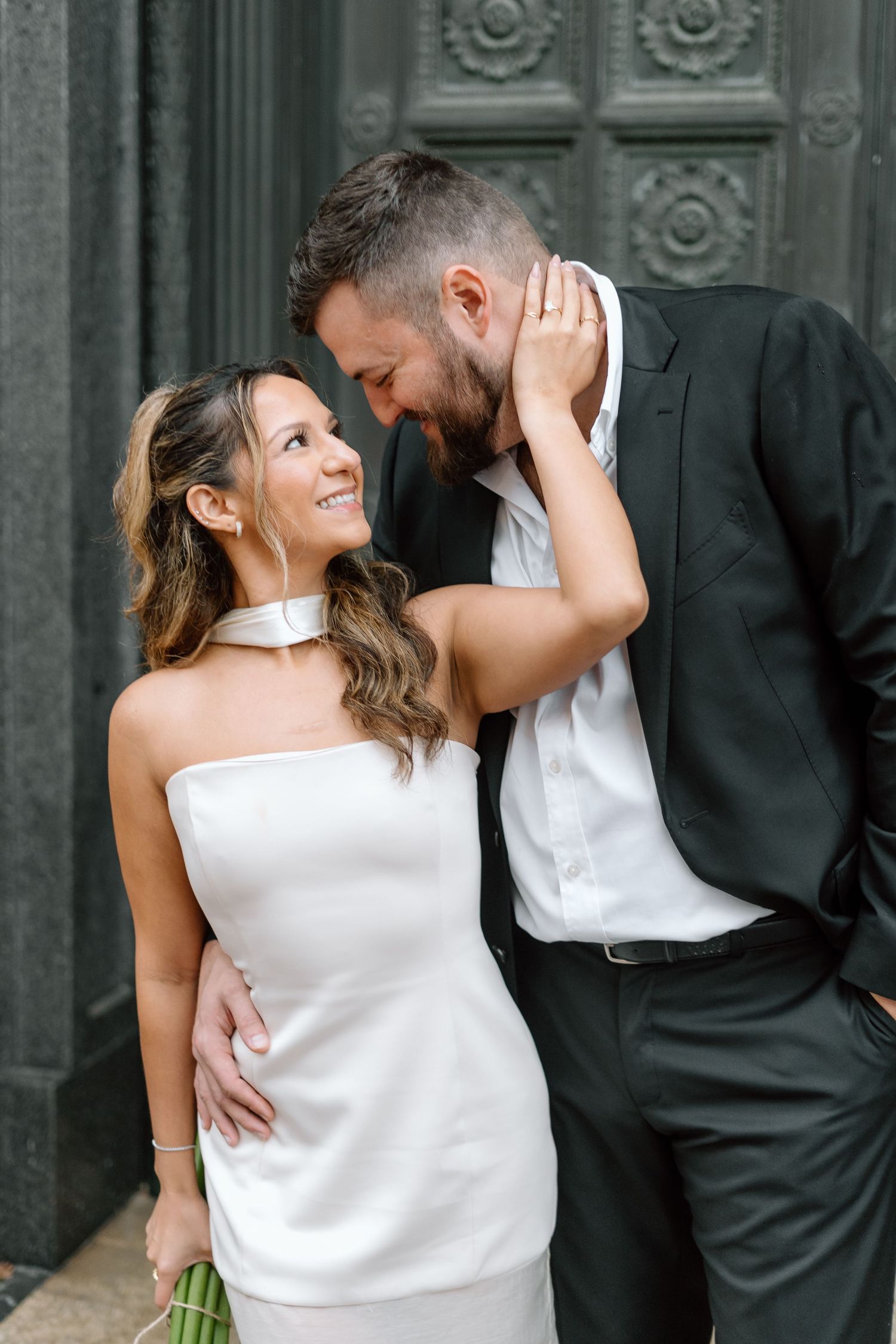 Romantic wedding couple poses intimately against an ornate stone wall backdrop.