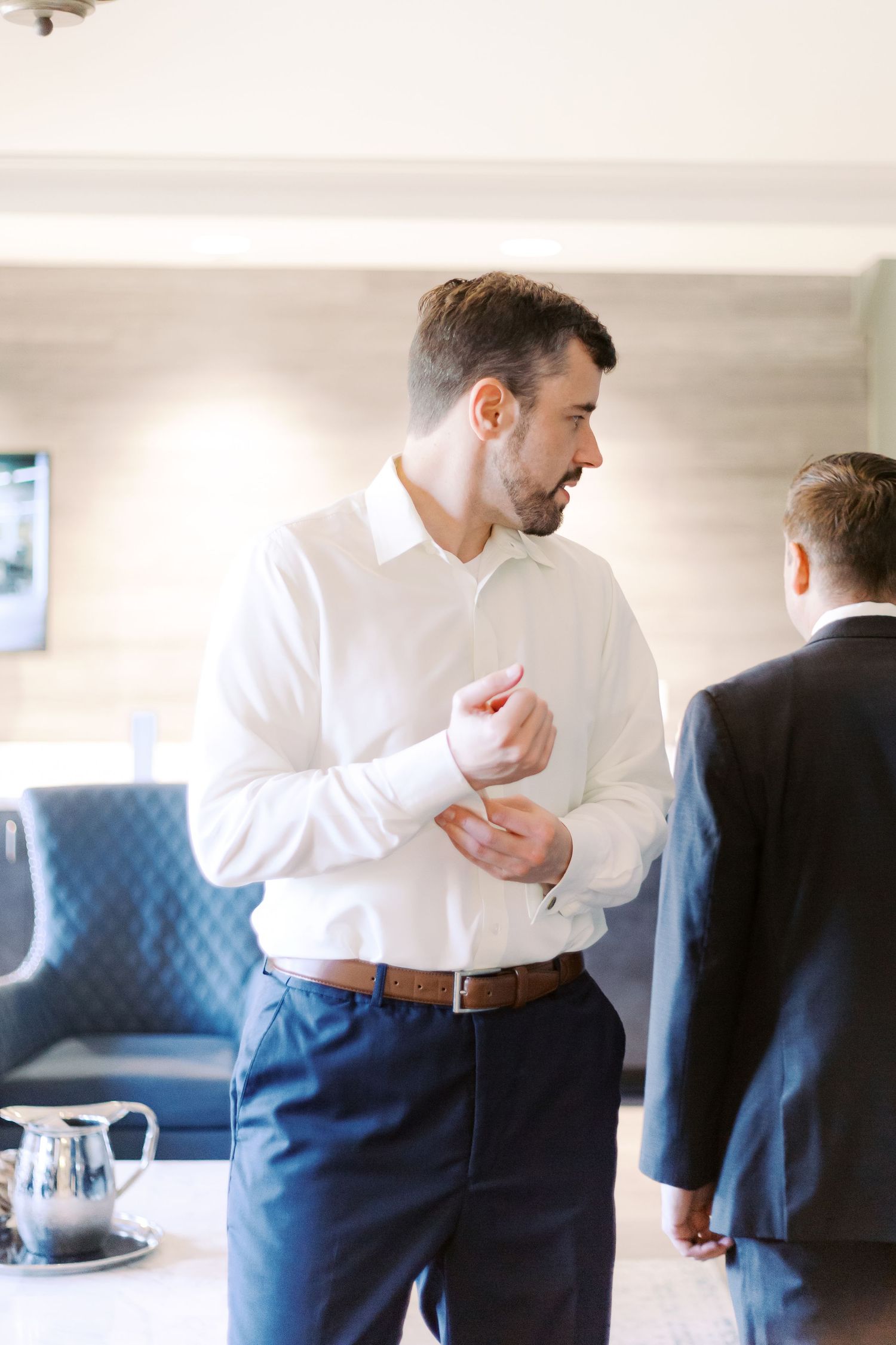 Men in formal attire gather and chat during what appears to be a wedding preparation.