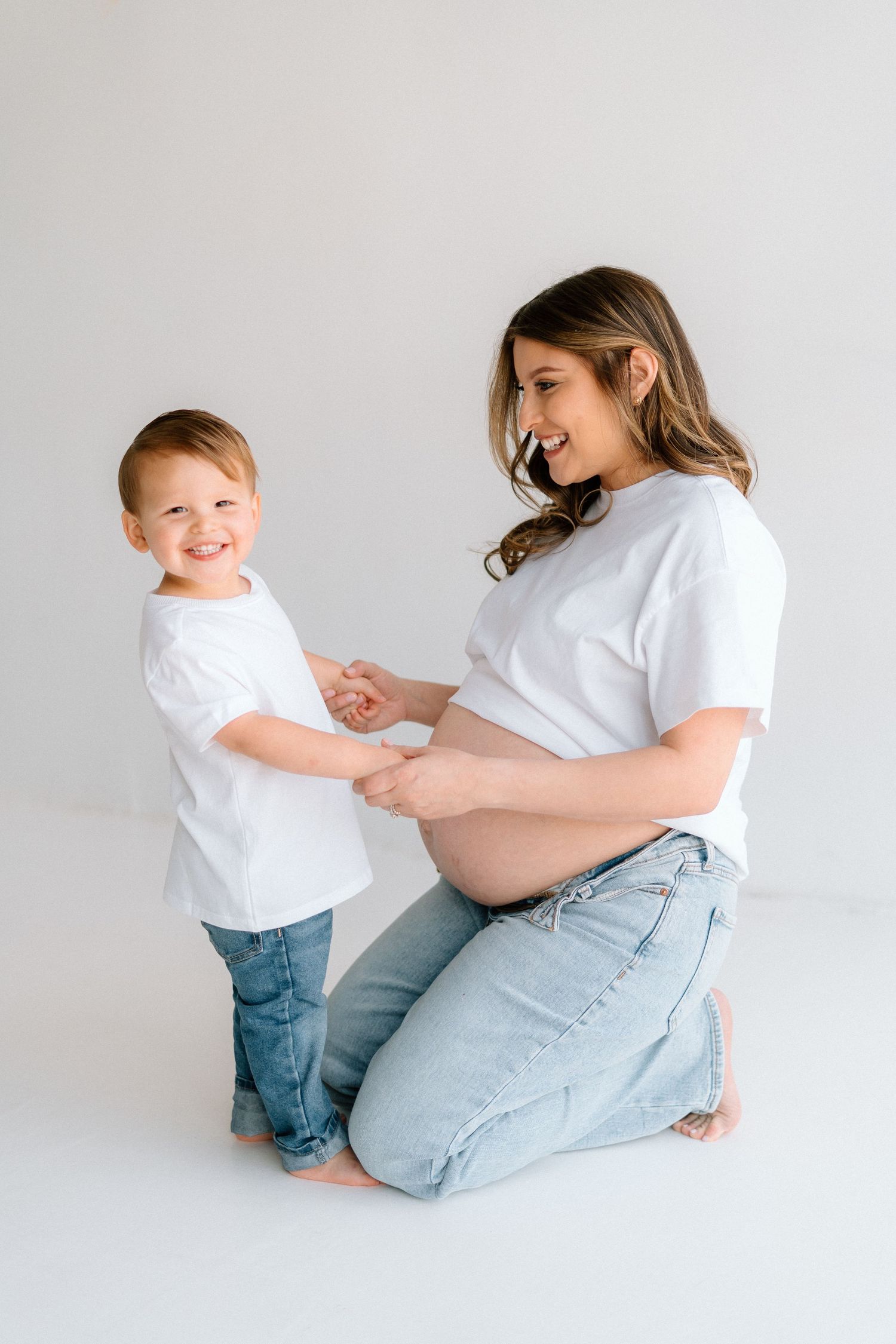 Candid family moments captured in white studio setting showing pregnancy and toddler interaction.