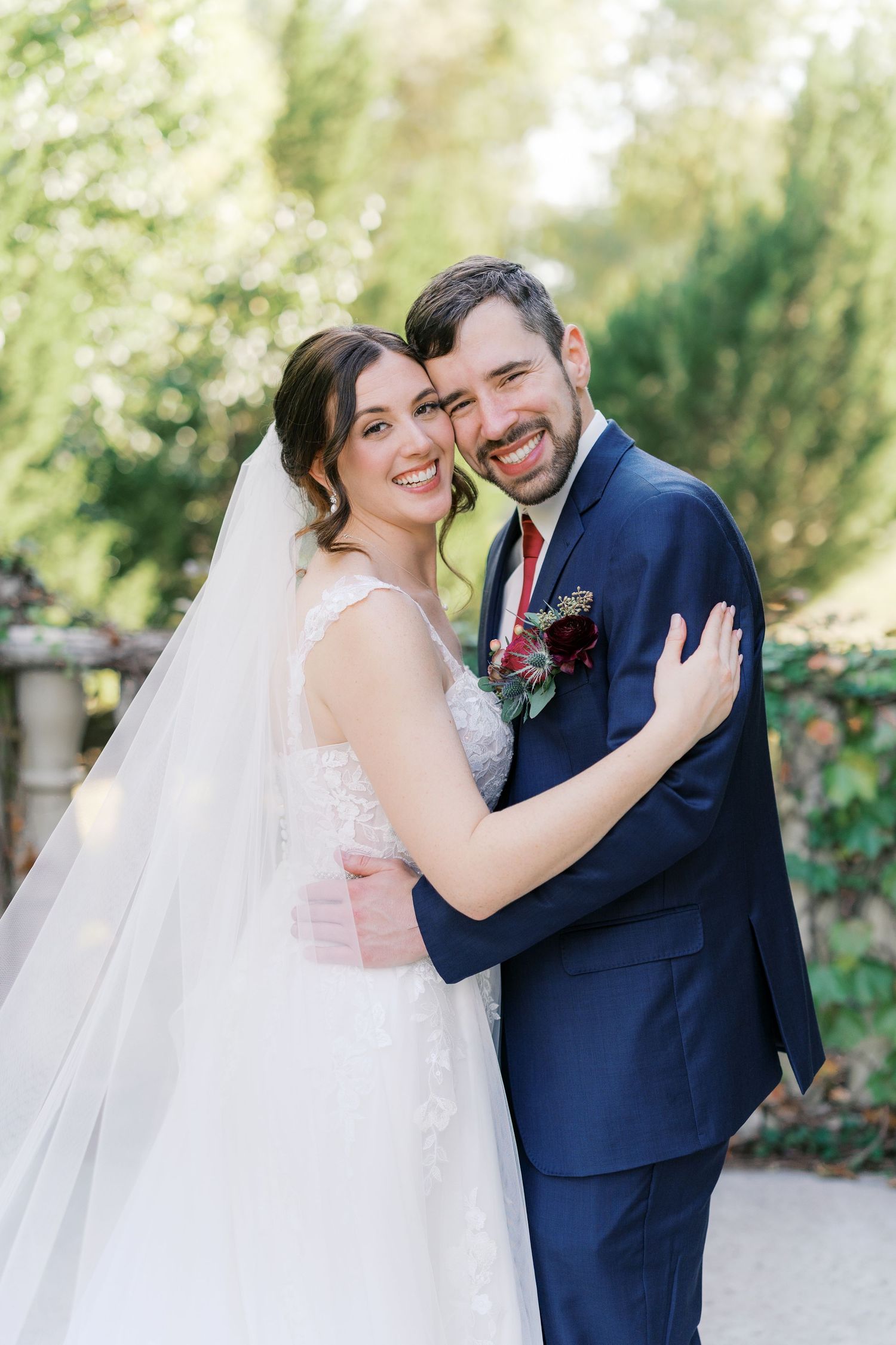 Joyful wedding couple embraces outdoors surrounded by lush garden greenery.