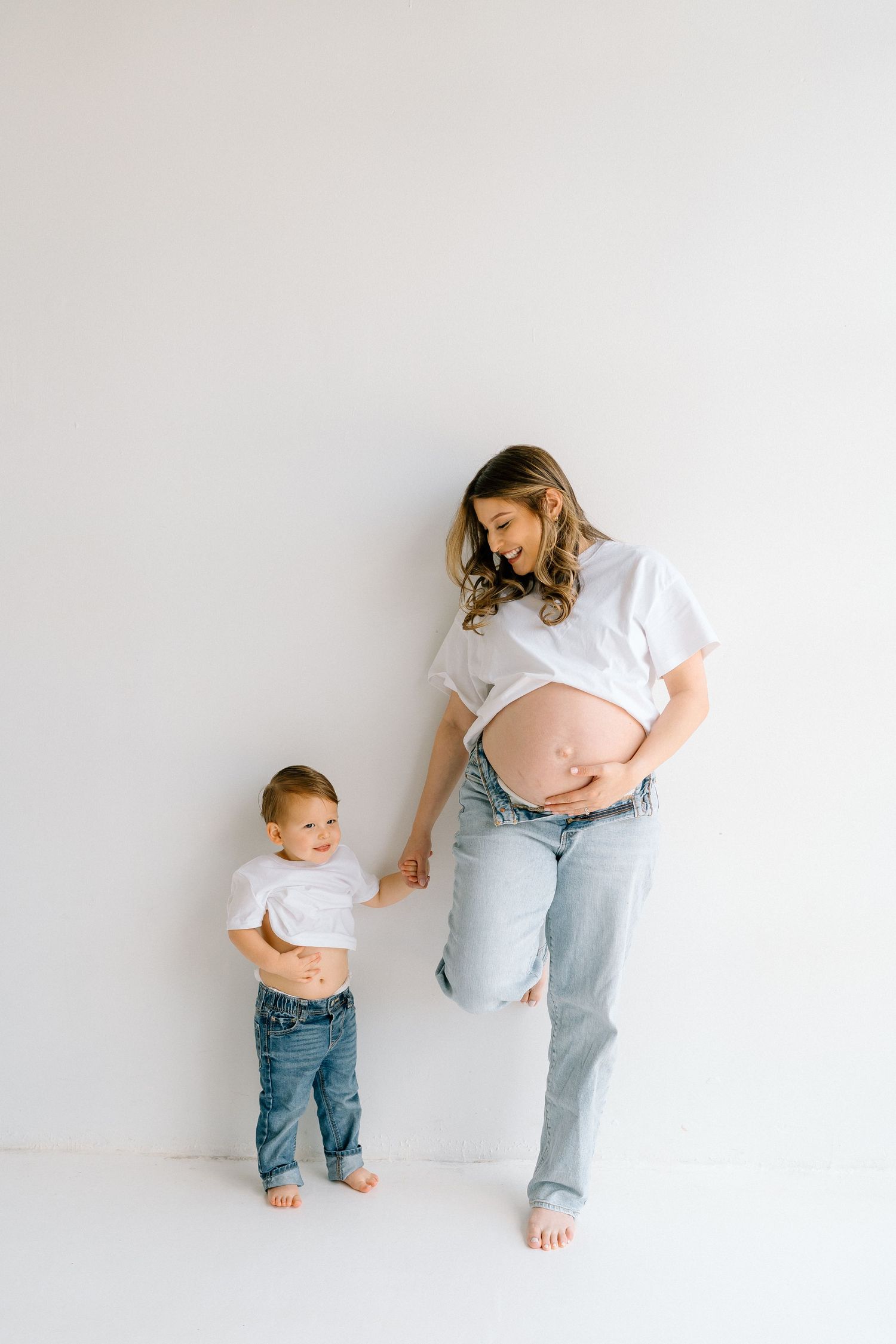 Simple studio maternity photos with family in coordinated casual outfits against white background.