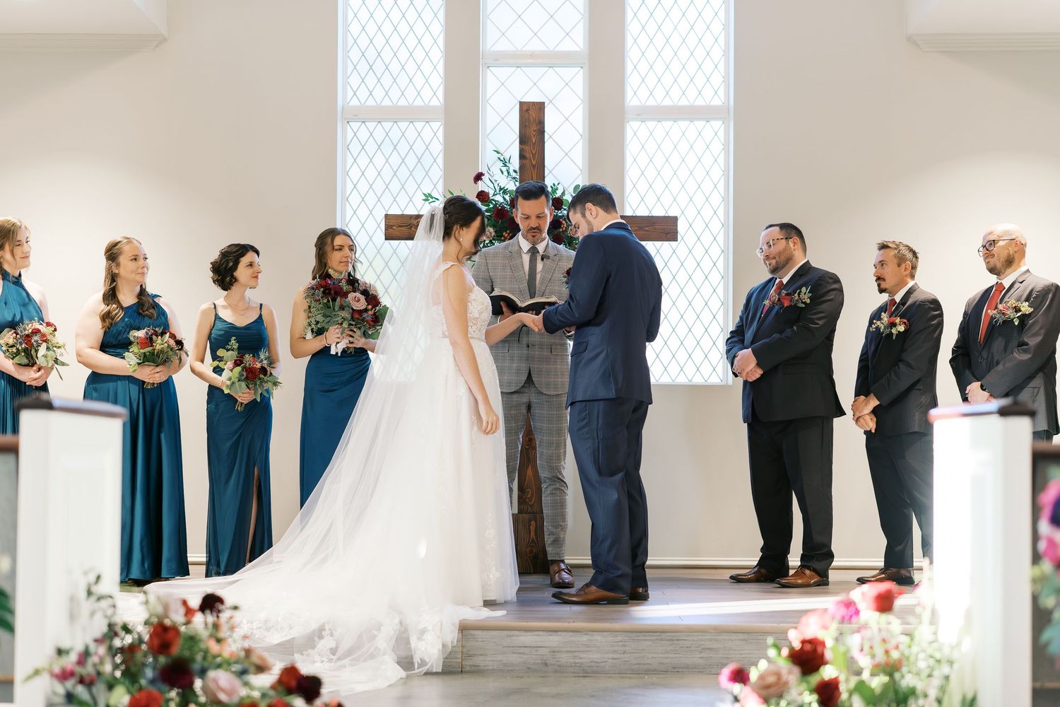 Wedding ceremony in a bright white chapel with teal-dressed attendants and floral decorations.