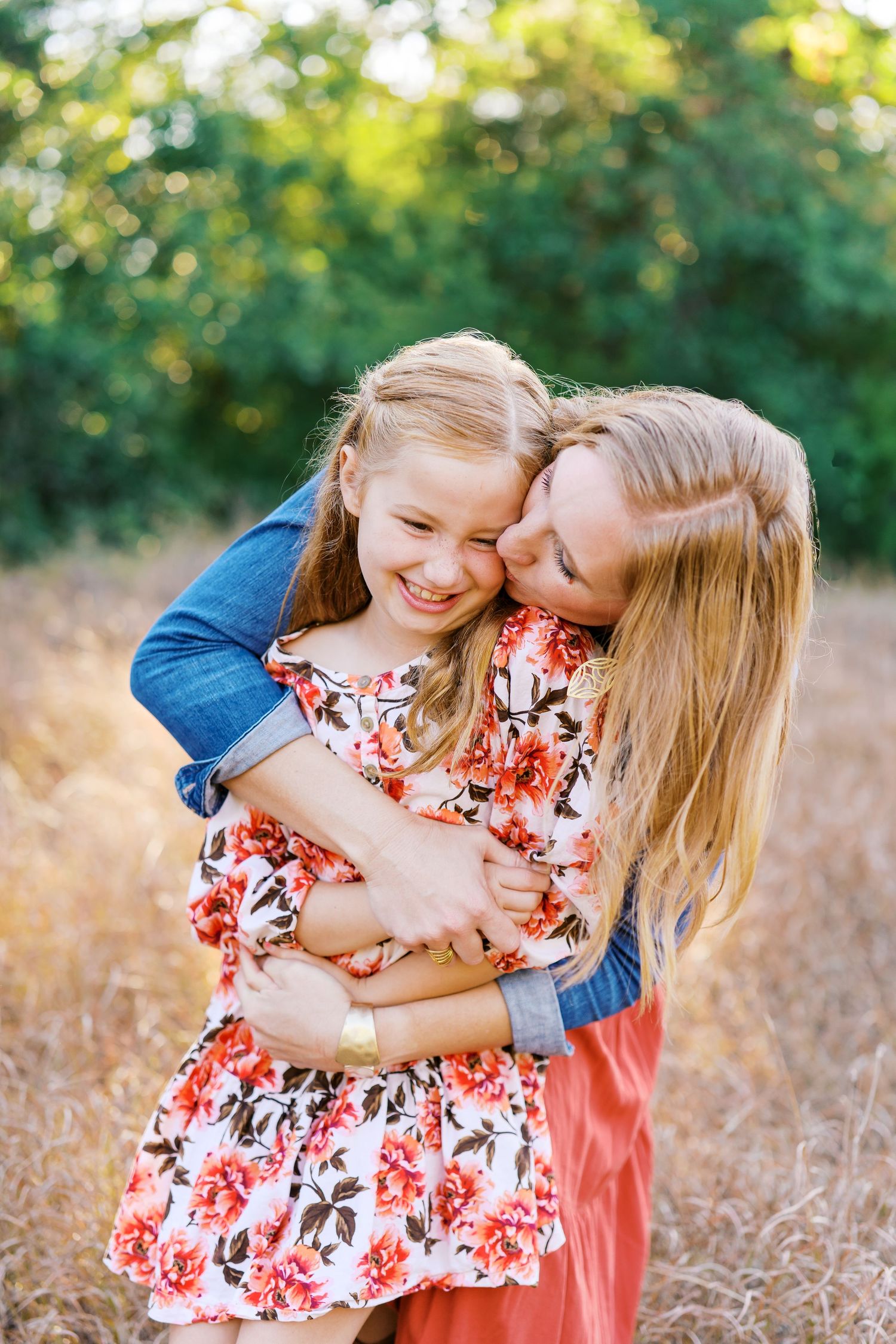 Two people share joyful moments together in a field during golden hour, wearing blue and floral outfits.