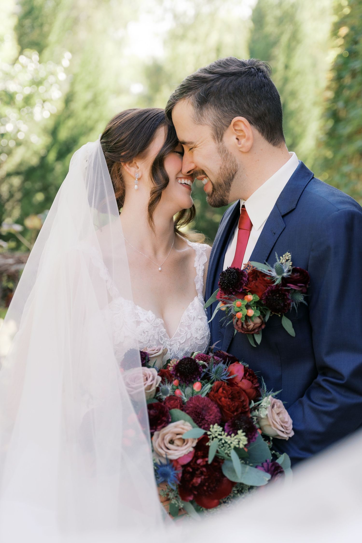 Romantic wedding portrait with deep red bouquet against navy suit and white dress.