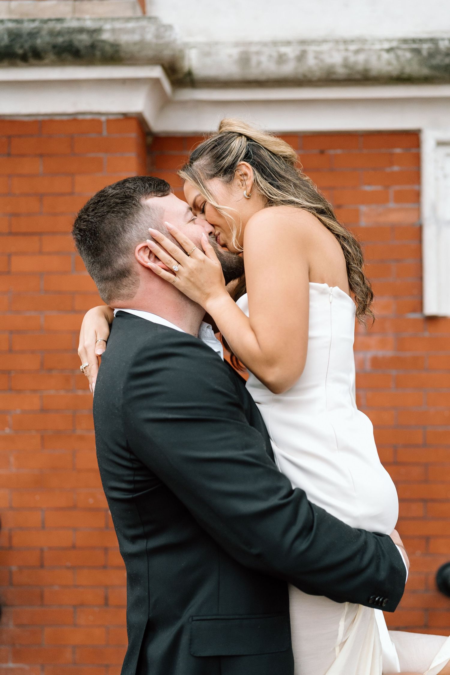 Romantic wedding couple embraces against rustic brick wall background.