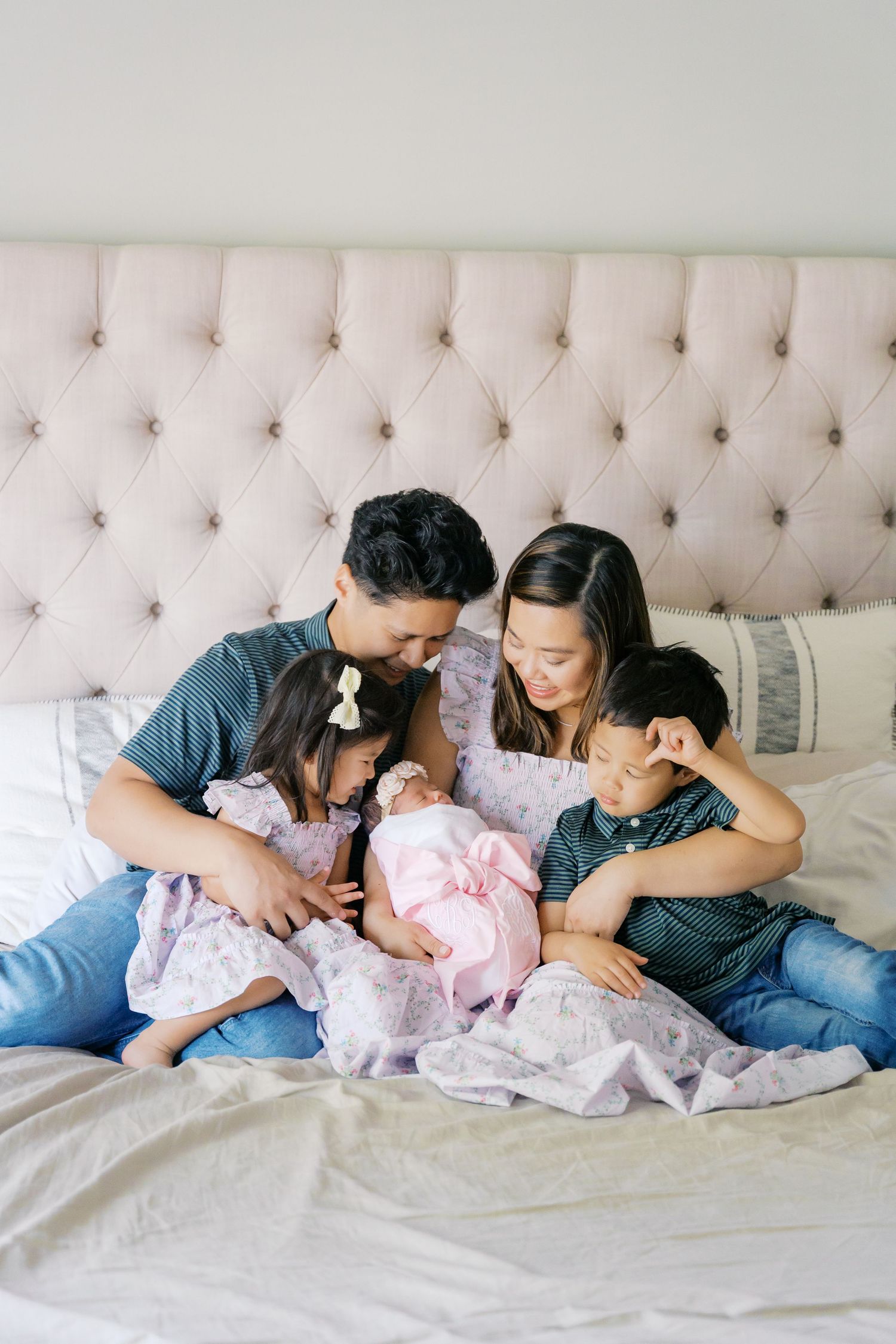 Family relaxing together on a tufted bed while bonding with their newborn.