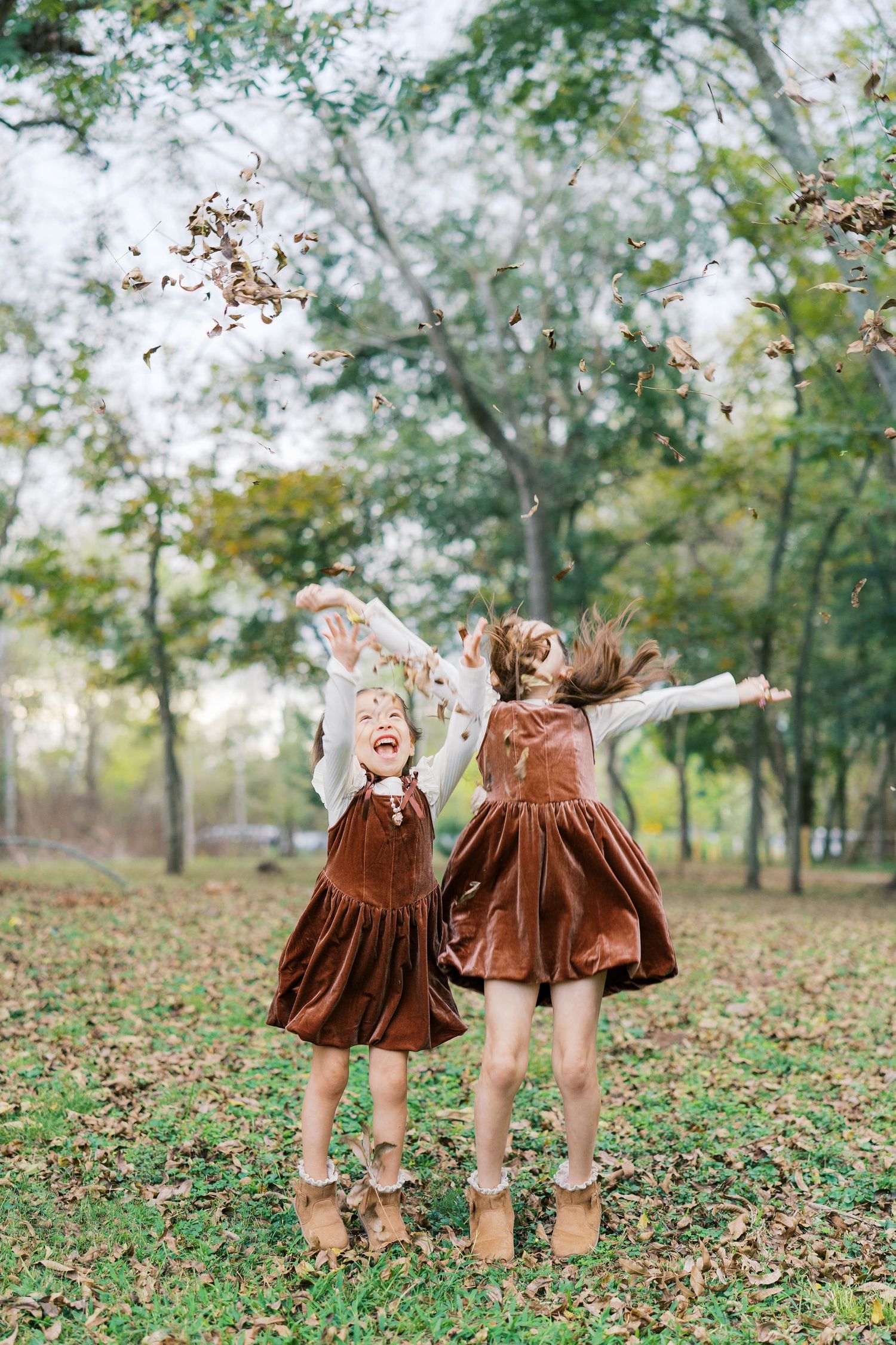 Children in brown velvet dresses playing and twirling in a leafy autumn park setting.