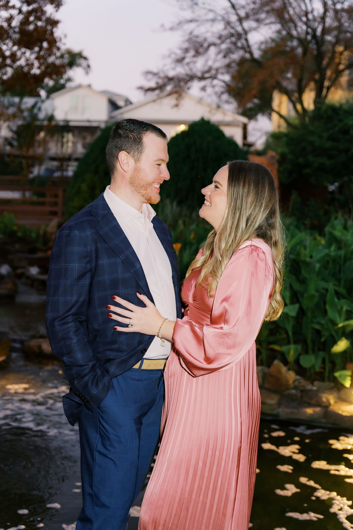 Evening engagement photoshoot by a garden pond with ambient lighting.