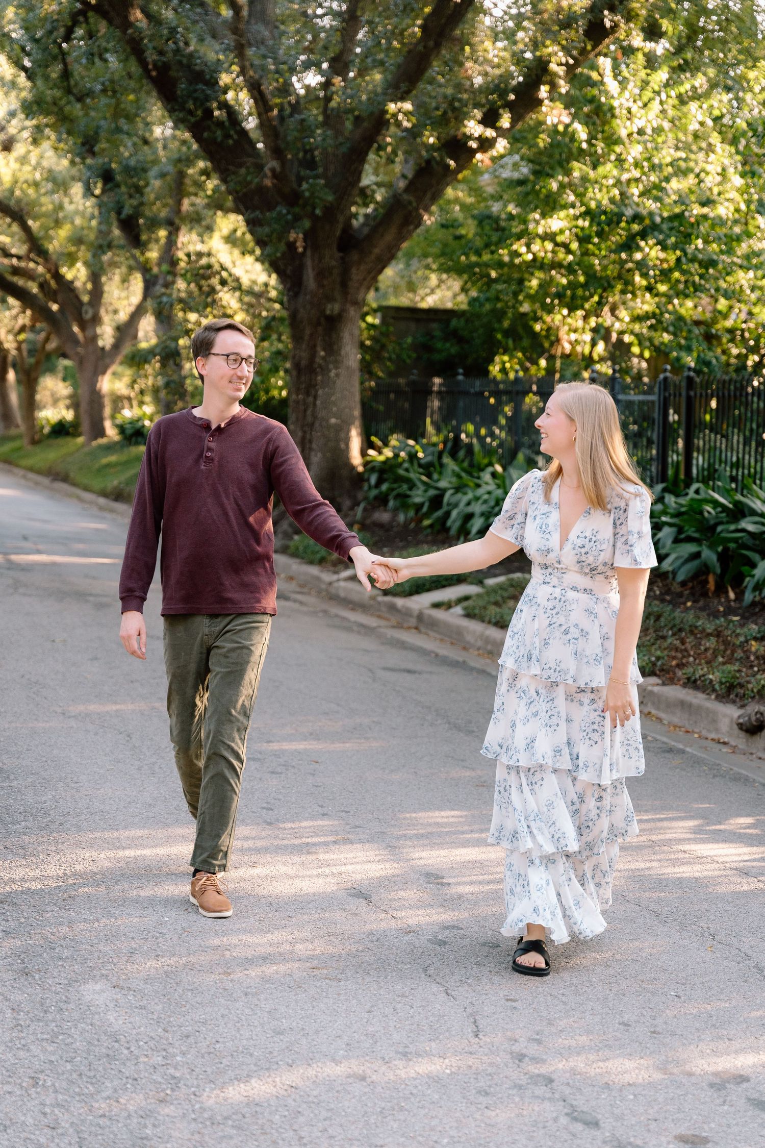 A couple takes romantic photos on a tree-lined path during golden hour.