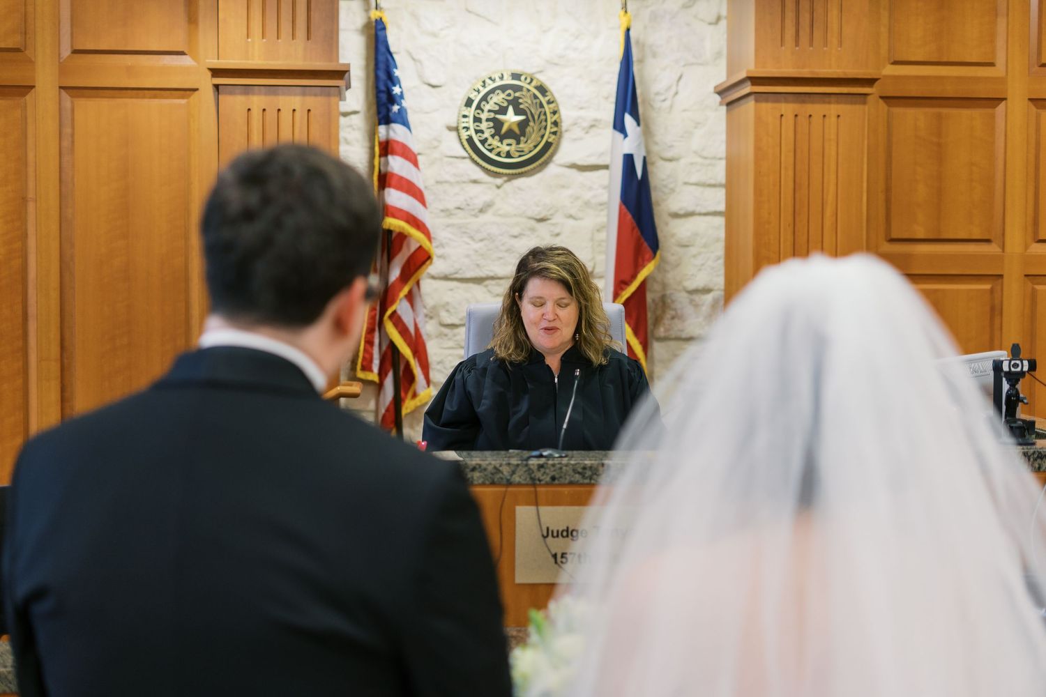 Wedding ceremony taking place in a wood-paneled courtroom with American flags.