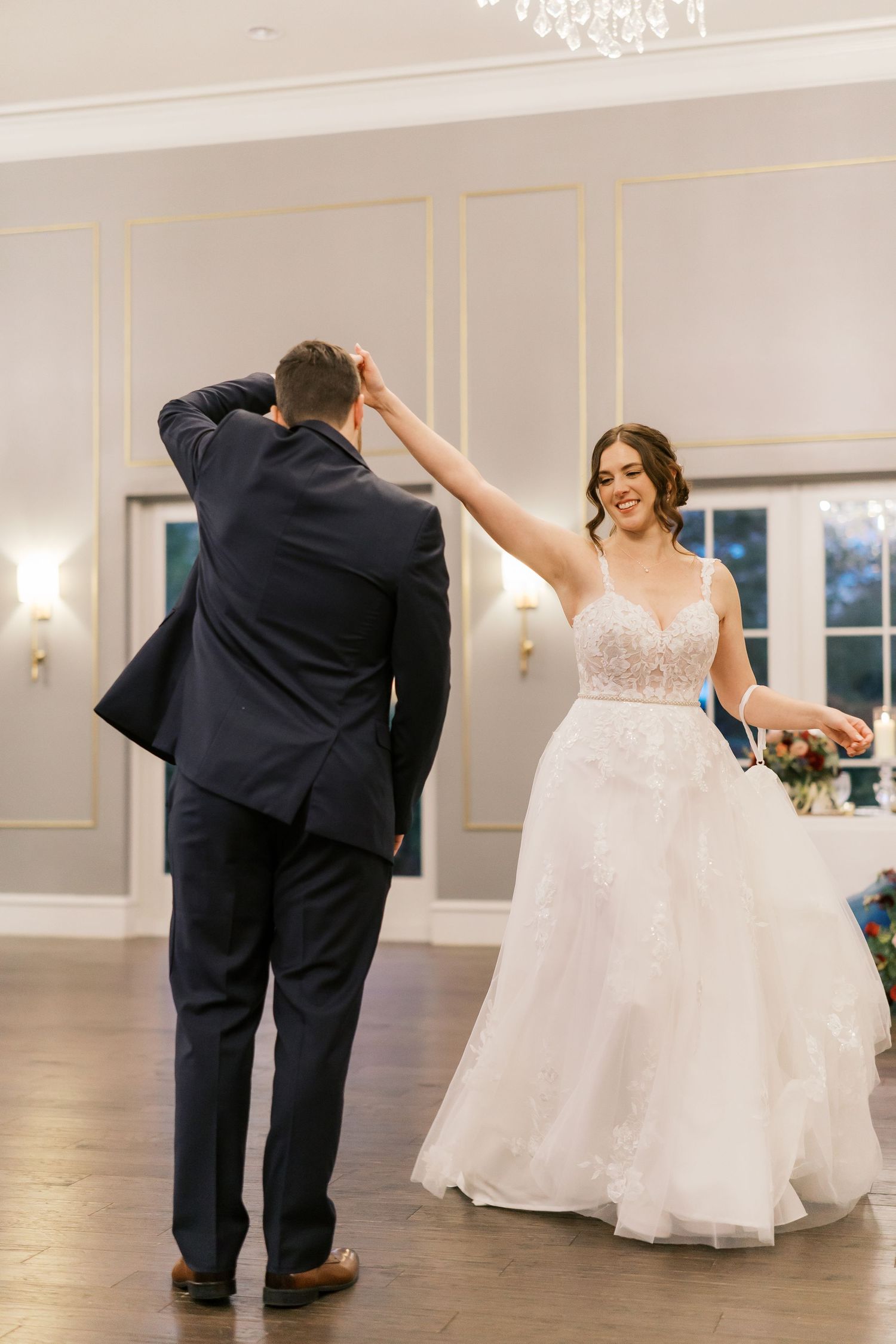 Wedding couple dancing in an elegant ballroom with white and gold decor.