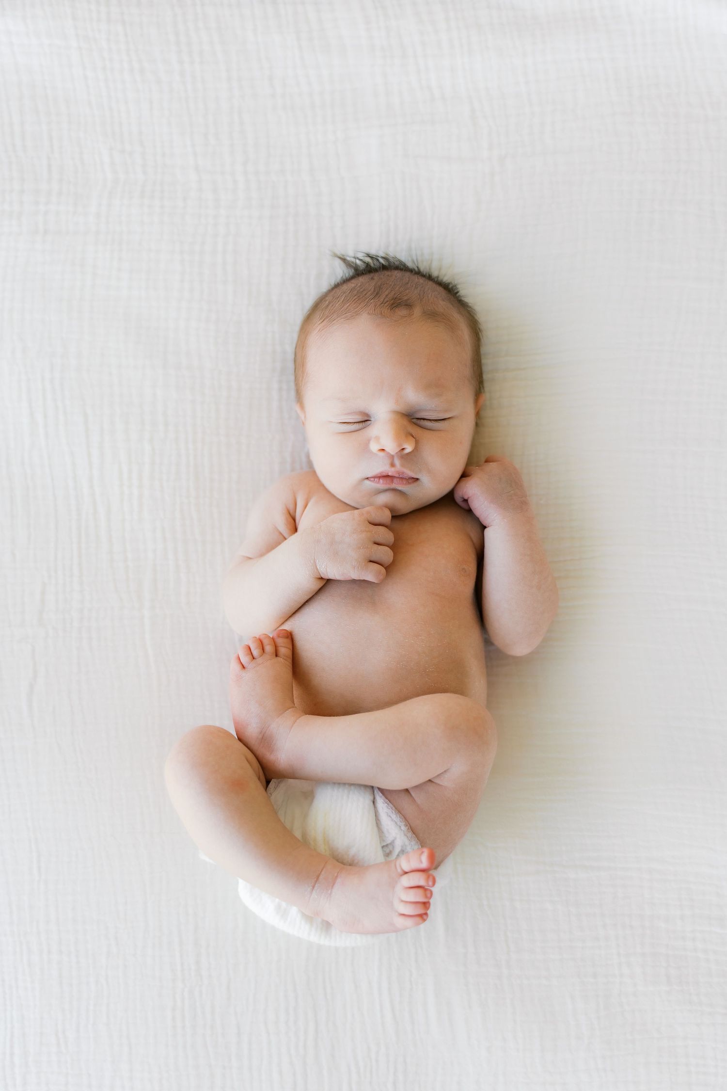 A sleeping newborn baby lies peacefully on a white blanket in various relaxed poses.