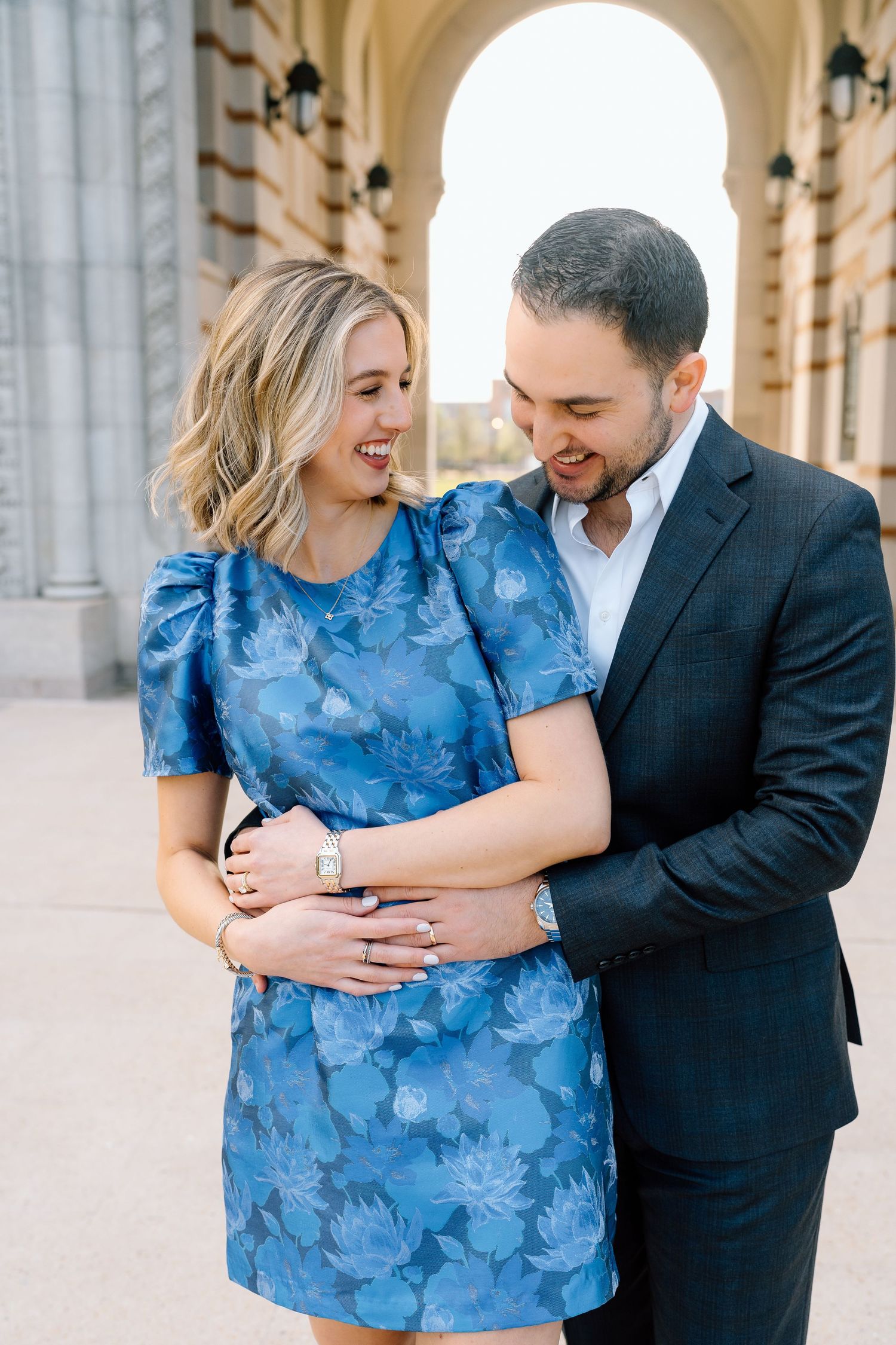 Couple embracing and laughing under arched colonnade in formal attire.