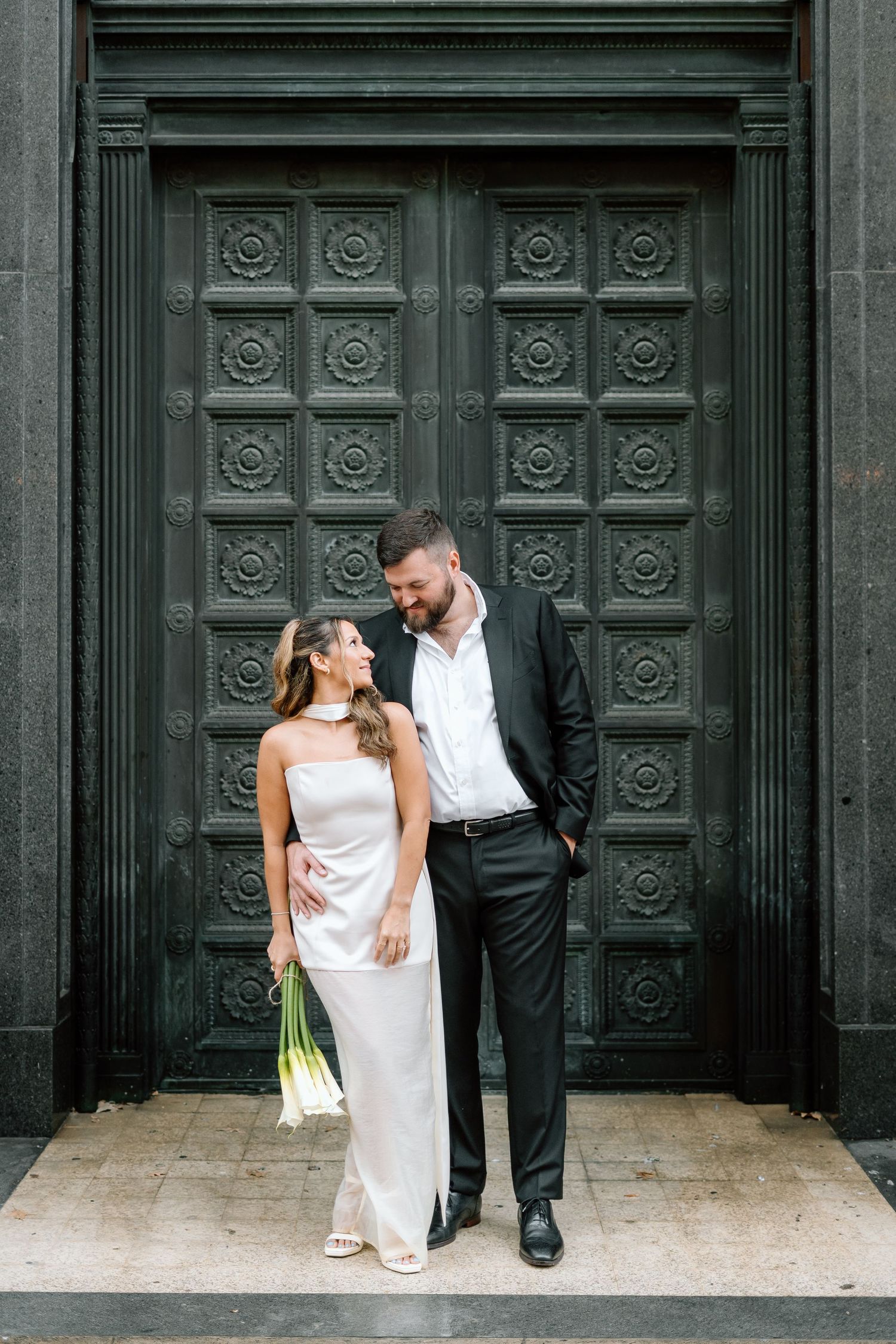 Wedding couple shares intimate moment in front of decorative black doors.