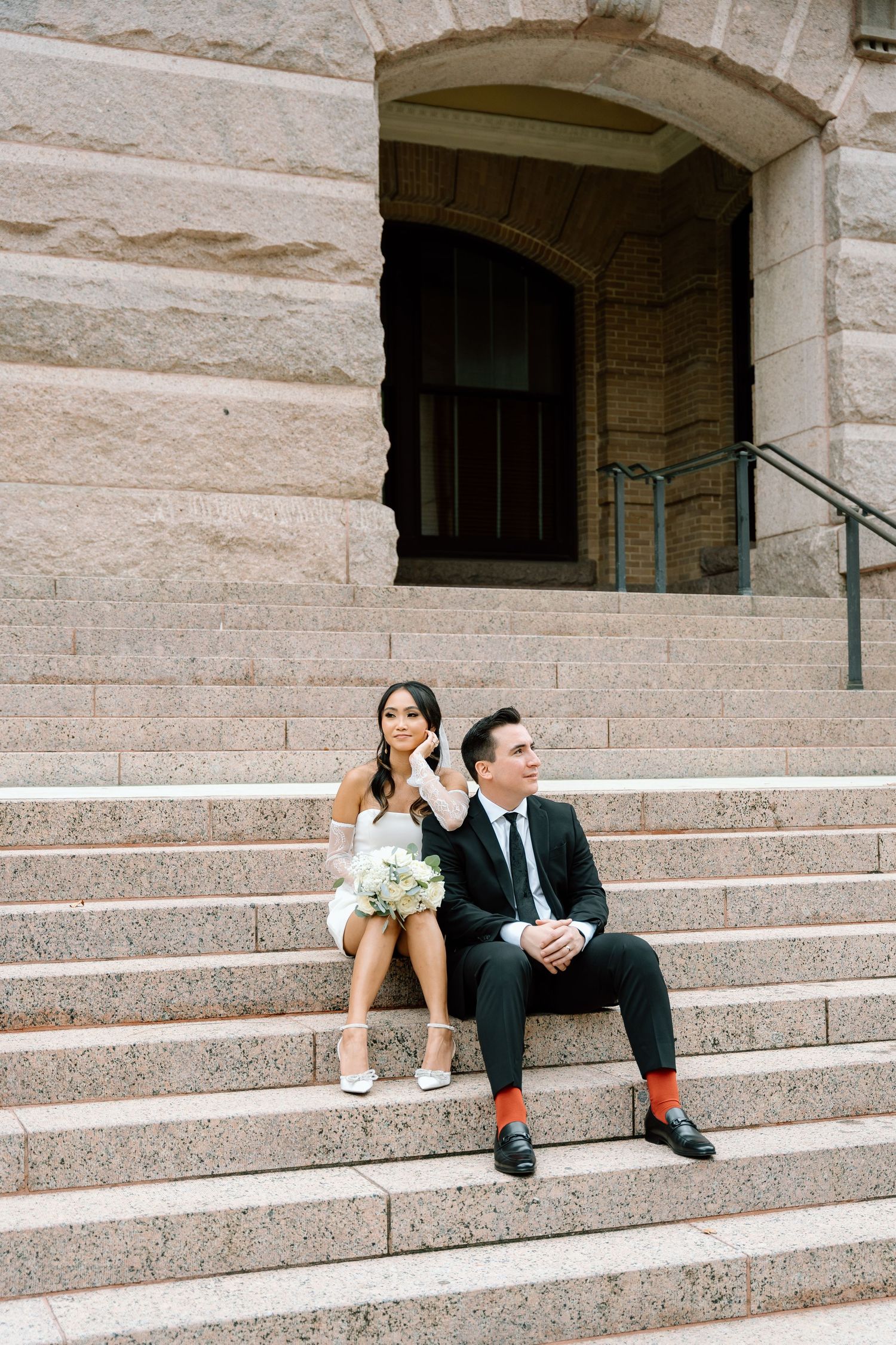 Wedding couple relaxing on stone steps of historic building.