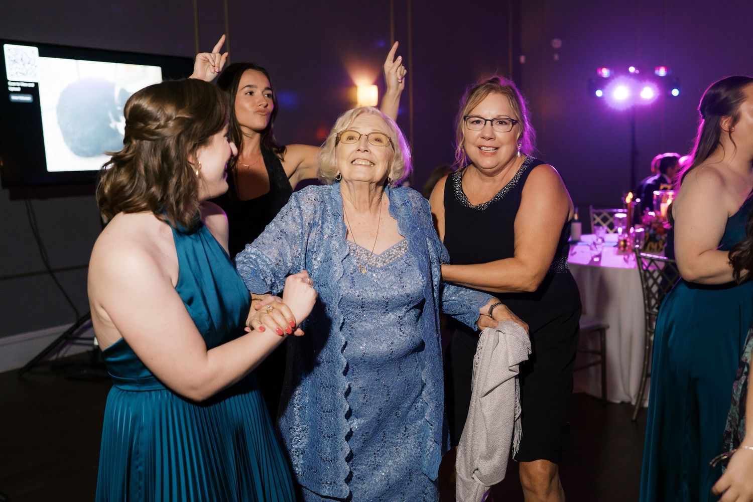 Wedding reception dance floor with guests enjoying the celebration under purple lighting.