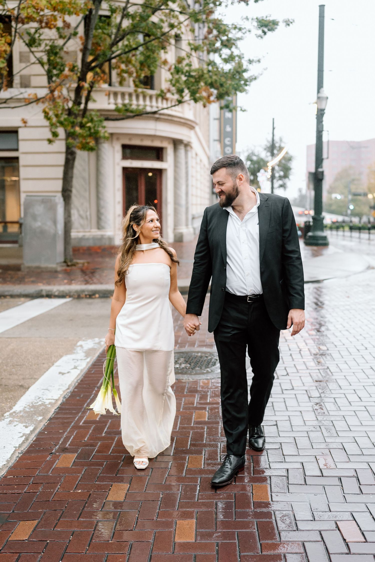 Couple walks along wet brick sidewalk in downtown area.